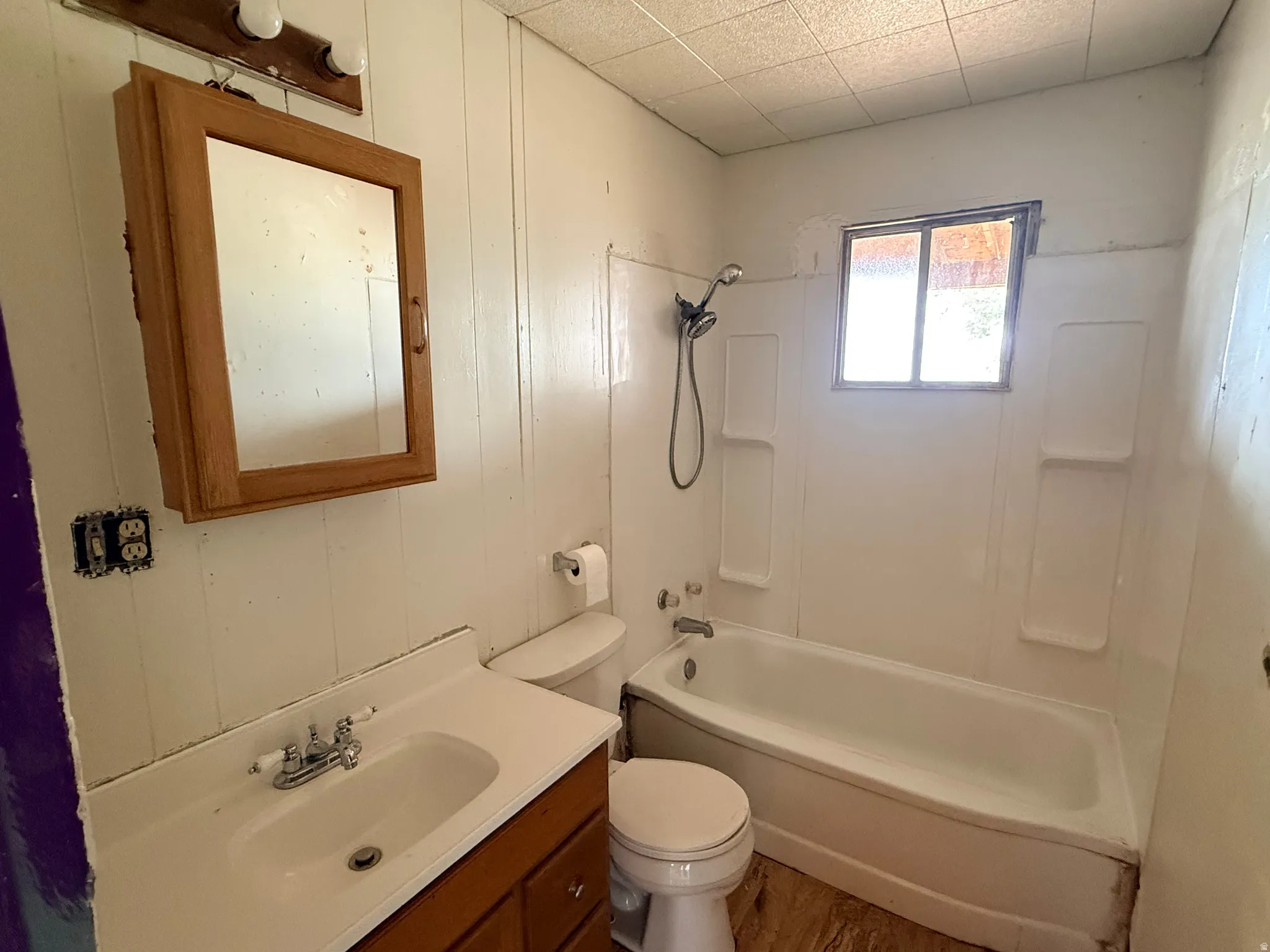 Bathroom with a white vanity sink, a wood-finish medicine cabinet, and a shower/tub combination with a wall-mounted showerhead