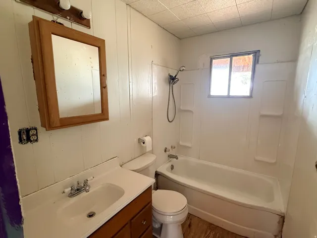 Bathroom with a white vanity sink, a wood-finish medicine cabinet, and a shower/tub combination with a wall-mounted showerhead