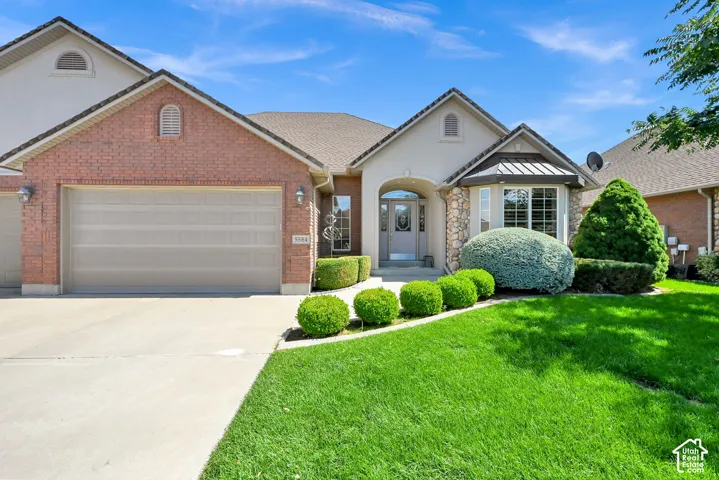 Brick and stucco exterior with stone accents, an arched entryway, a bay window, and a concrete driveway