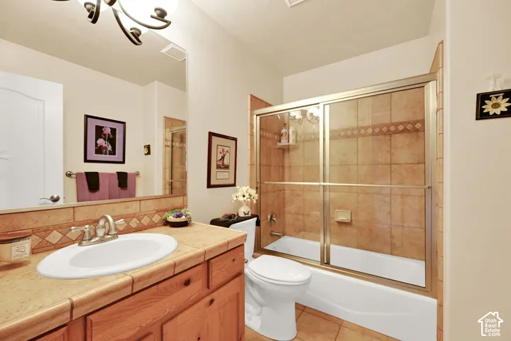 Bathroom featuring a tiled shower-tub combination with sliding glass doors, a vanity with a tiled countertop, and a built-in wood-finish cabinet