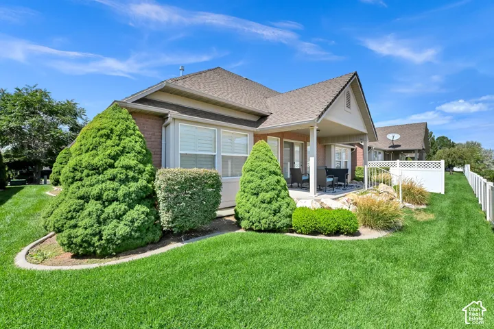 Manicured lawn with a covered patio, brick exterior, and white vinyl fencing