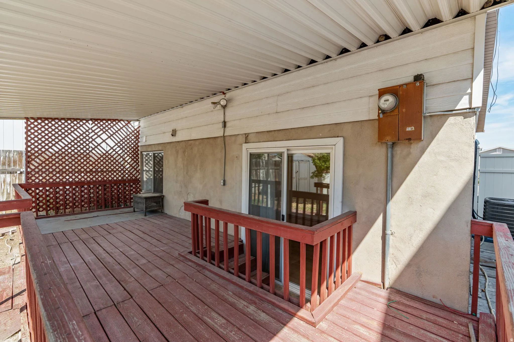 Covered wood deck with red-stained railing, featuring a sliding glass door and lattice privacy screen