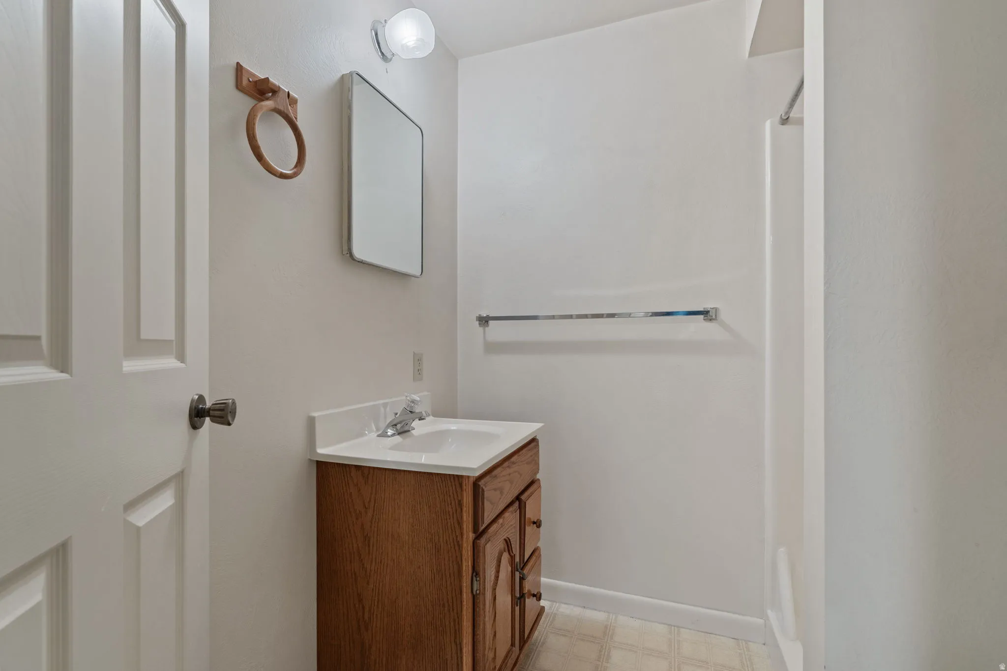 Bathroom featuring a wood-finish vanity with an integrated sink, wall-mounted mirror, and overhead lighting