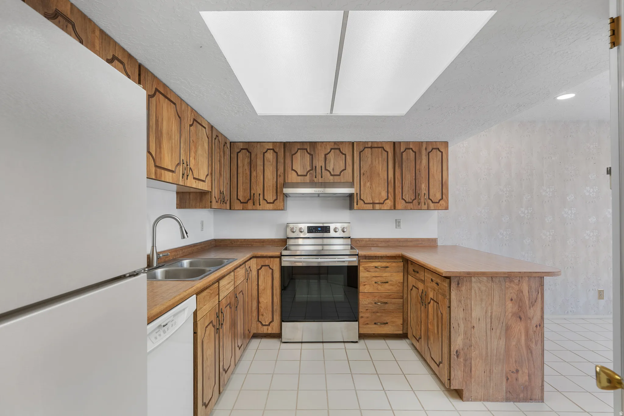U-shaped kitchen featuring wood cabinetry, stainless steel range, double basin sink, and white tile flooring