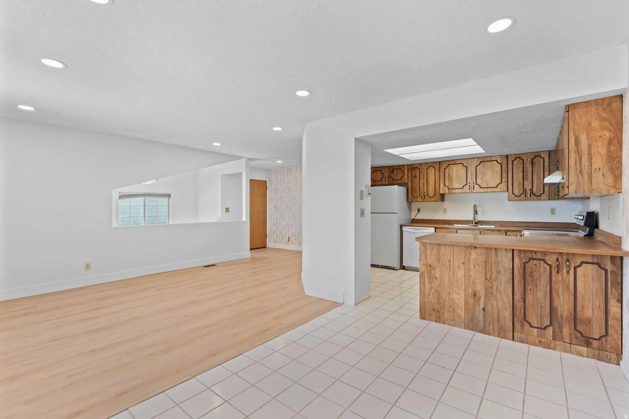 Recessed lighting, wood-finish flooring, white tile flooring, wood-finish cabinetry, and a skylight