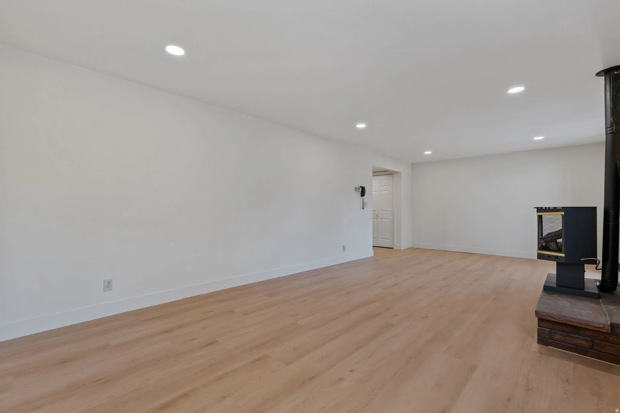 Wood-finish flooring, recessed lighting, white walls, and a freestanding fireplace with a brick base