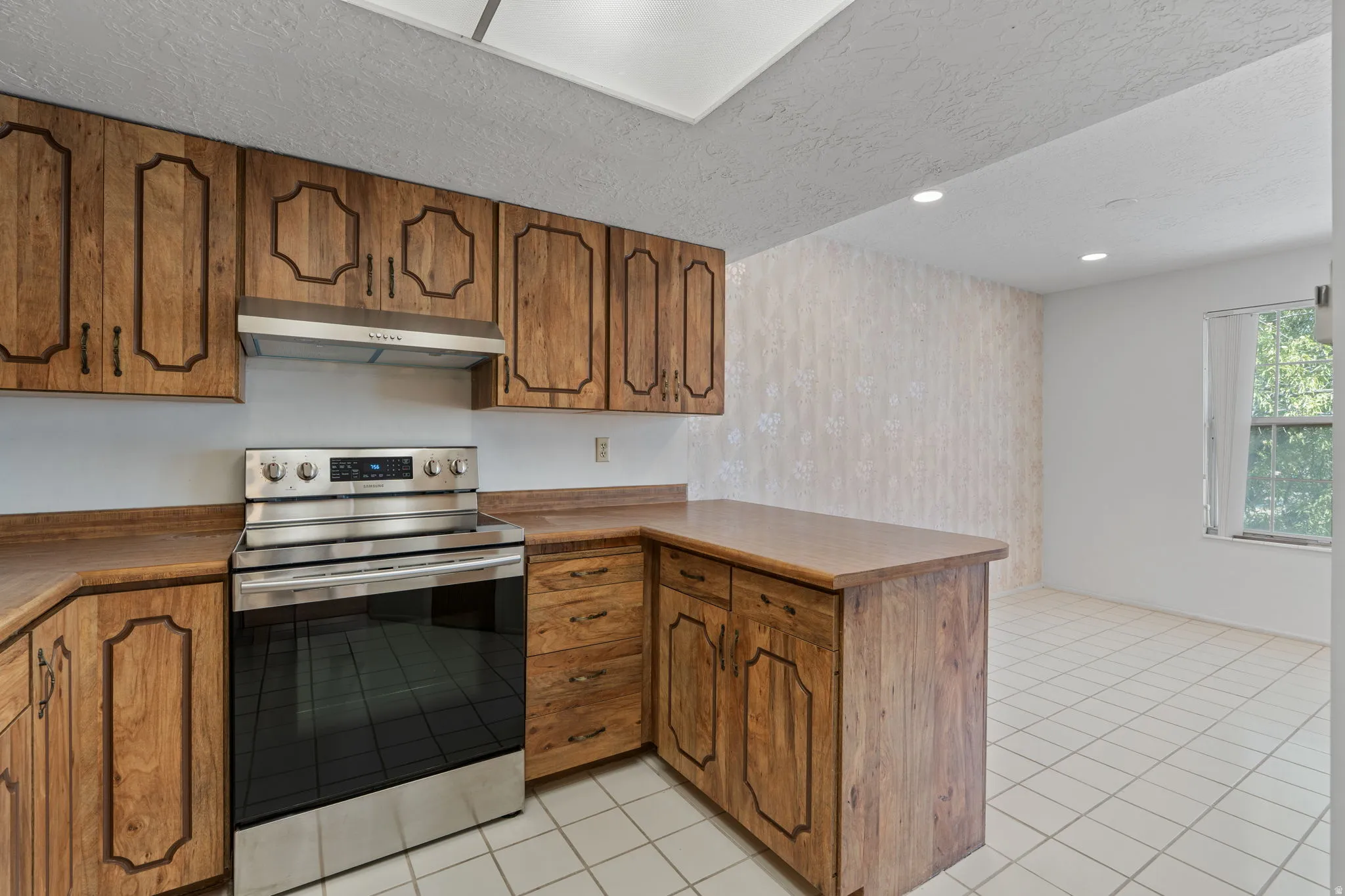 Wood-finish cabinetry, stainless steel range with overhead hood, wood-finish countertops, tile flooring, and recessed lighting