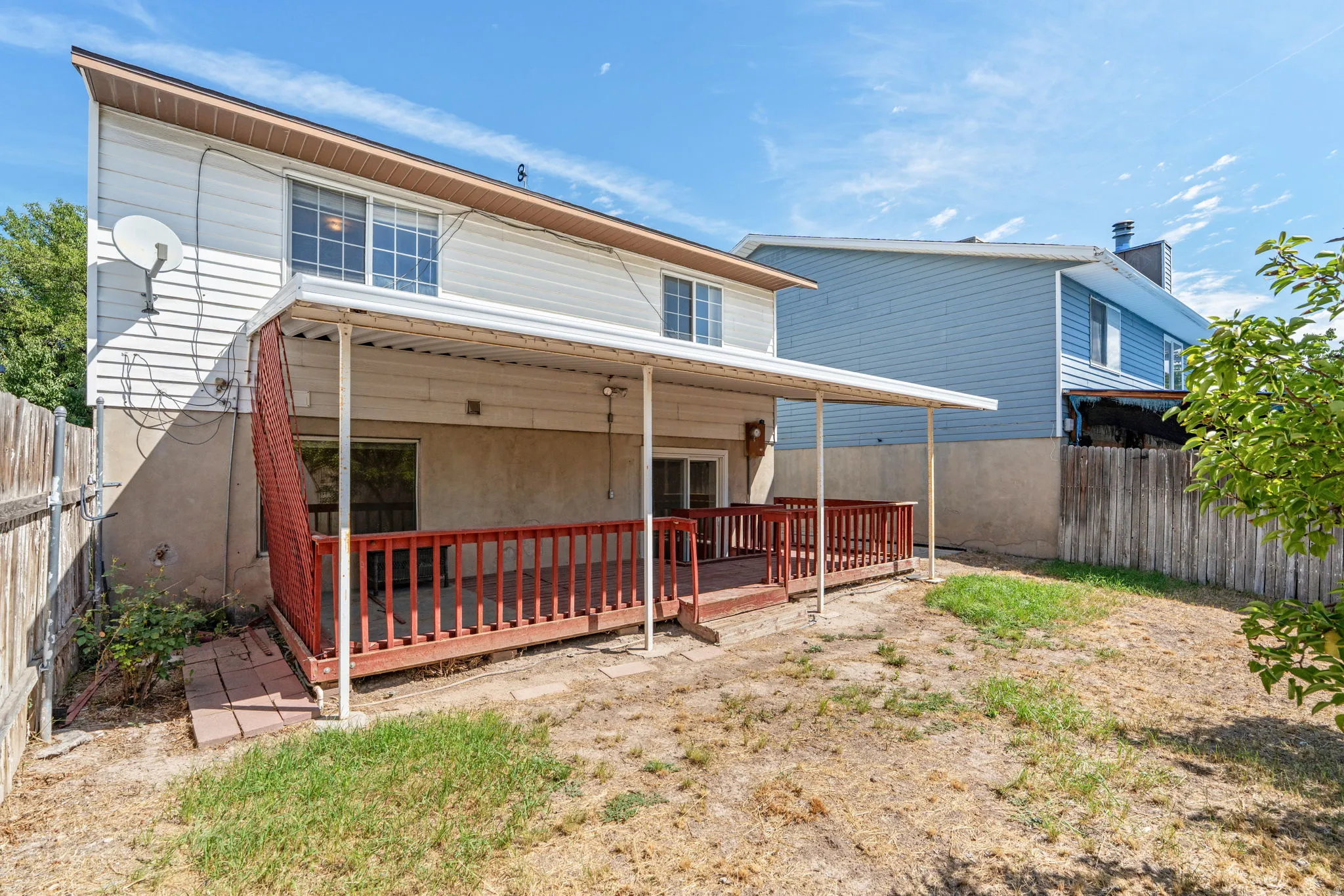 Rear exterior featuring a covered deck with red-stained wood railing, siding facade, and multiple windows