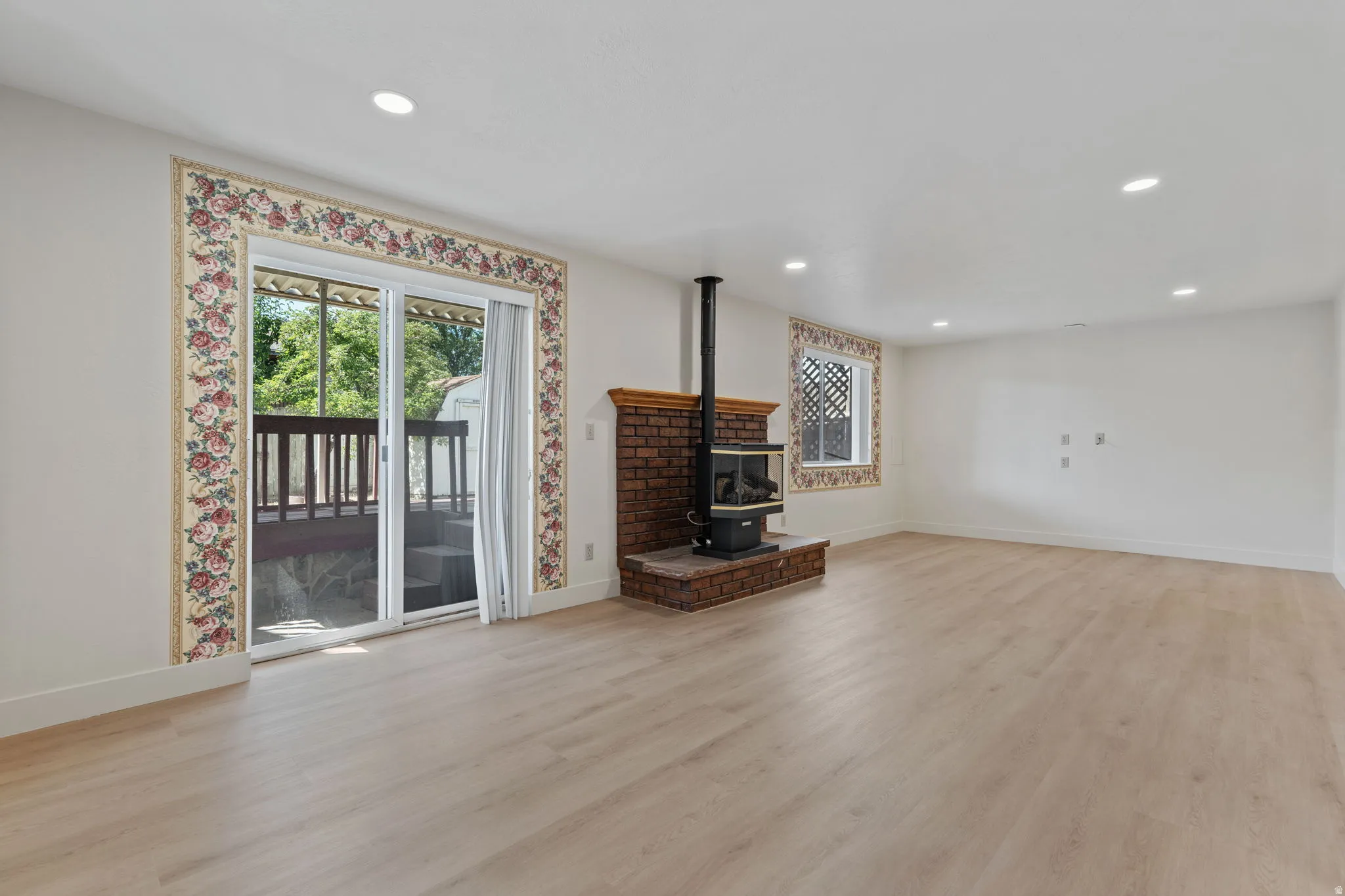 Wood-finish flooring throughout, recessed lighting, brick fireplace with a wood-burning stove, and a glass sliding door leading to an outdoor deck