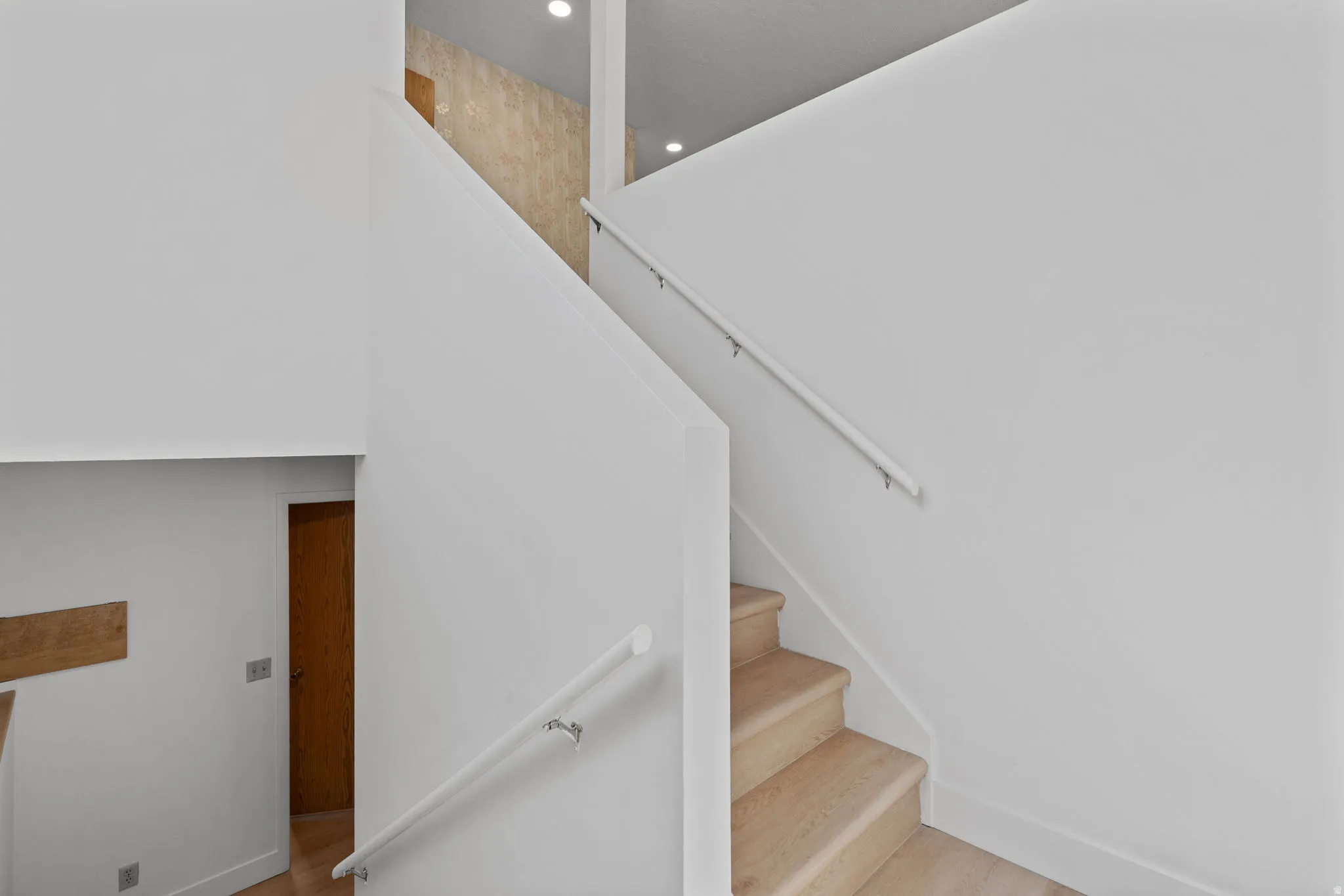 Wood-finish stairs with white risers and handrails, complemented by recessed lighting and light-colored walls