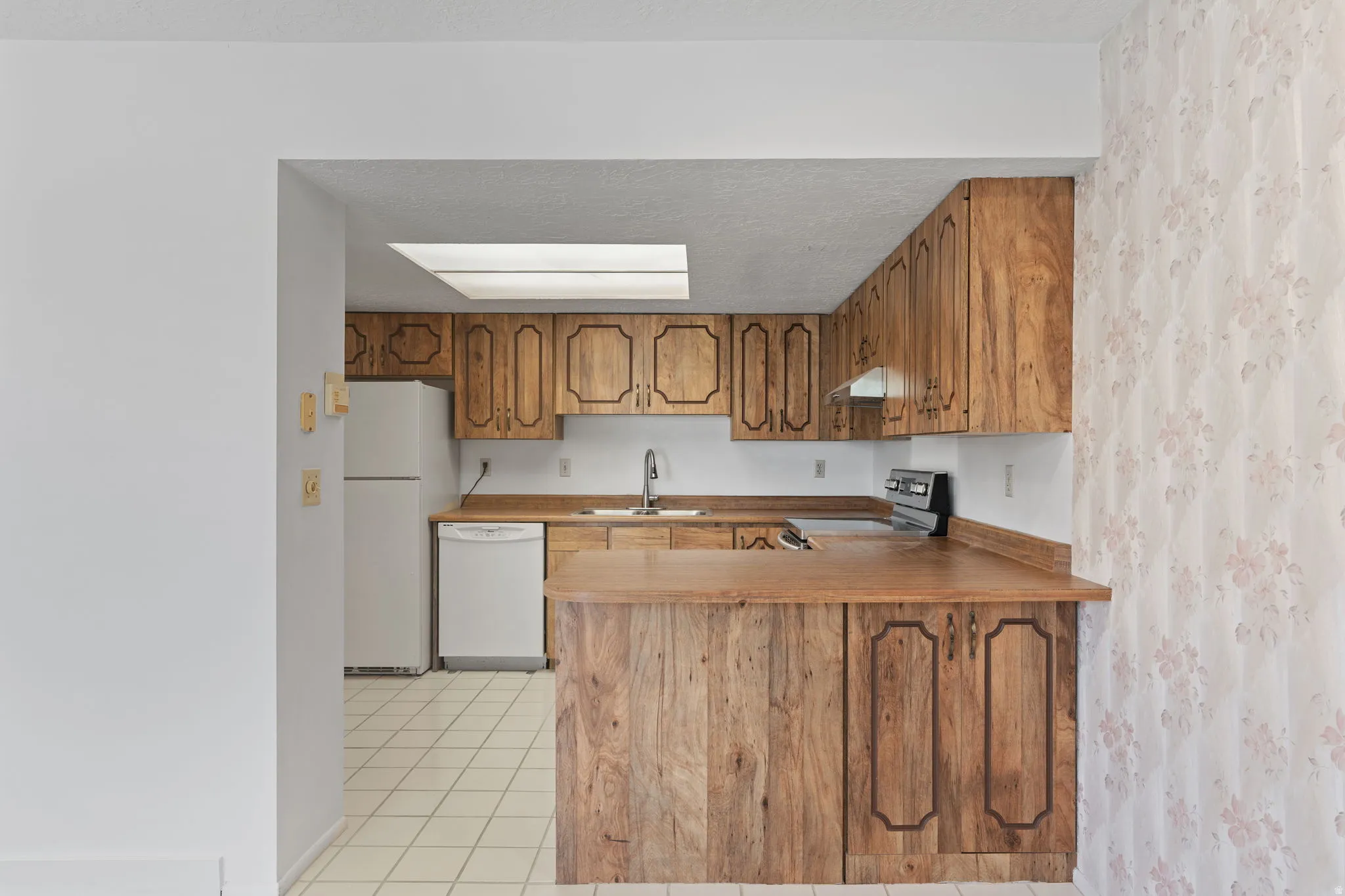 Kitchen featuring wood-finish cabinetry, solid surface countertops, a skylight, and white tile flooring