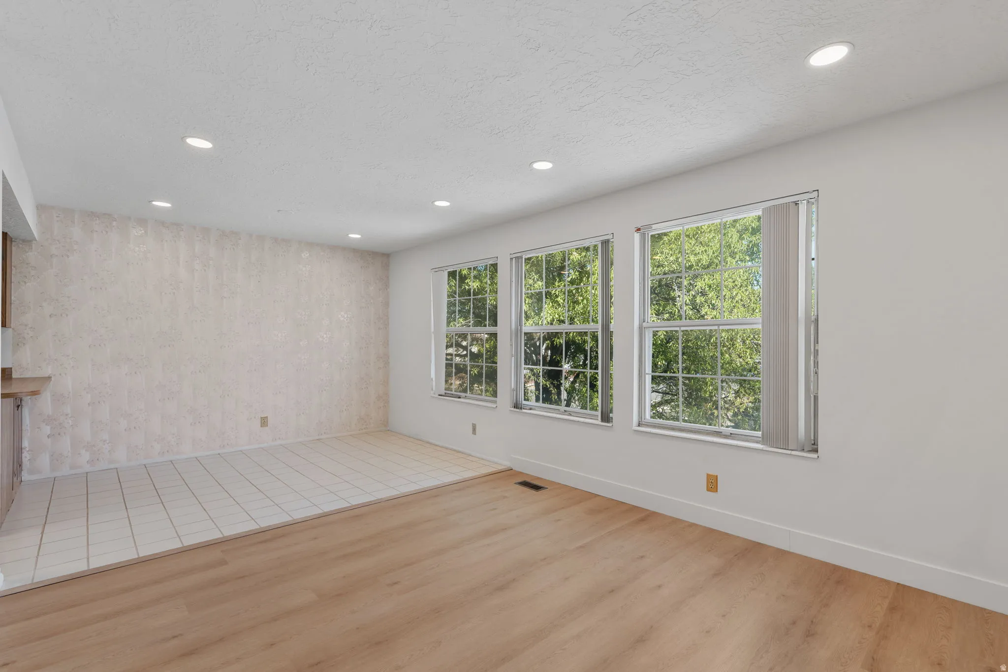 Recessed ceiling lighting, wood-finish flooring, white tiled flooring, three windows with vertical blinds, and a built-in wooden shelf