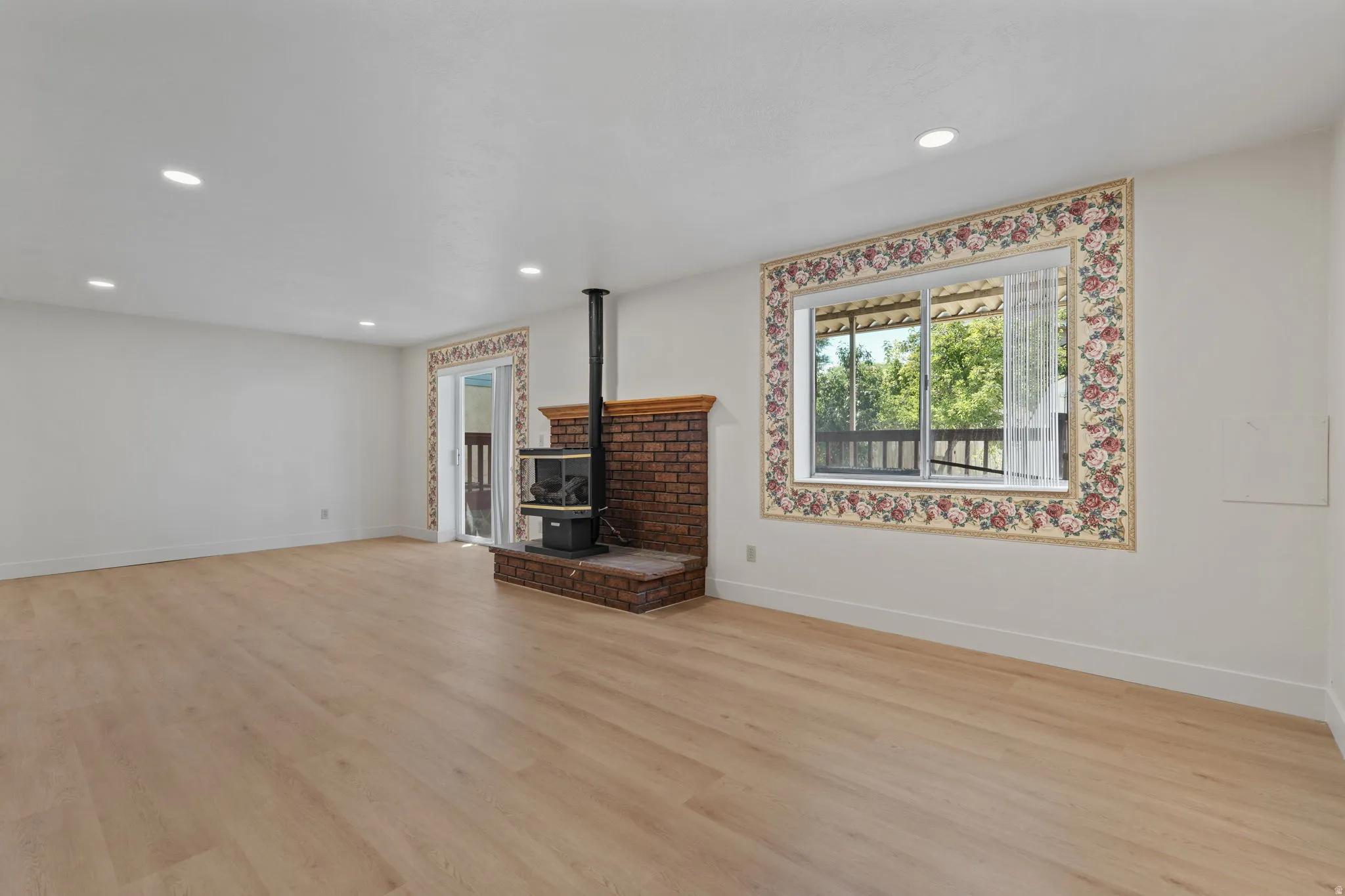 Expansive room with wood-finish flooring, a brick fireplace with a wood-burning stove, and recessed lighting