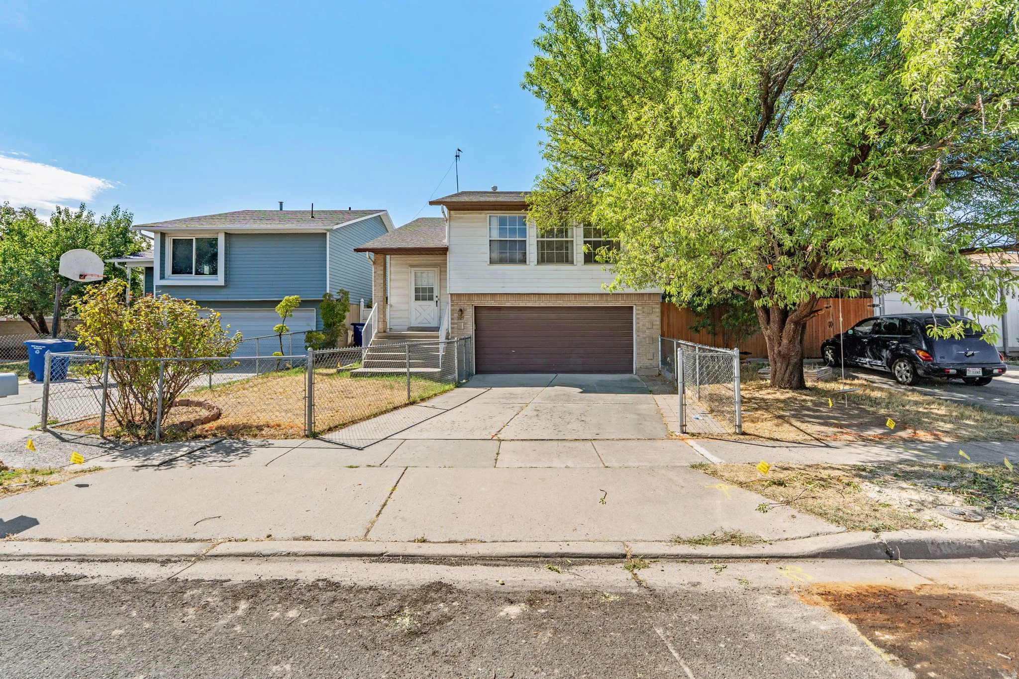 Two-story property with an attached garage, paved driveway, mature trees, and a chain-link fence