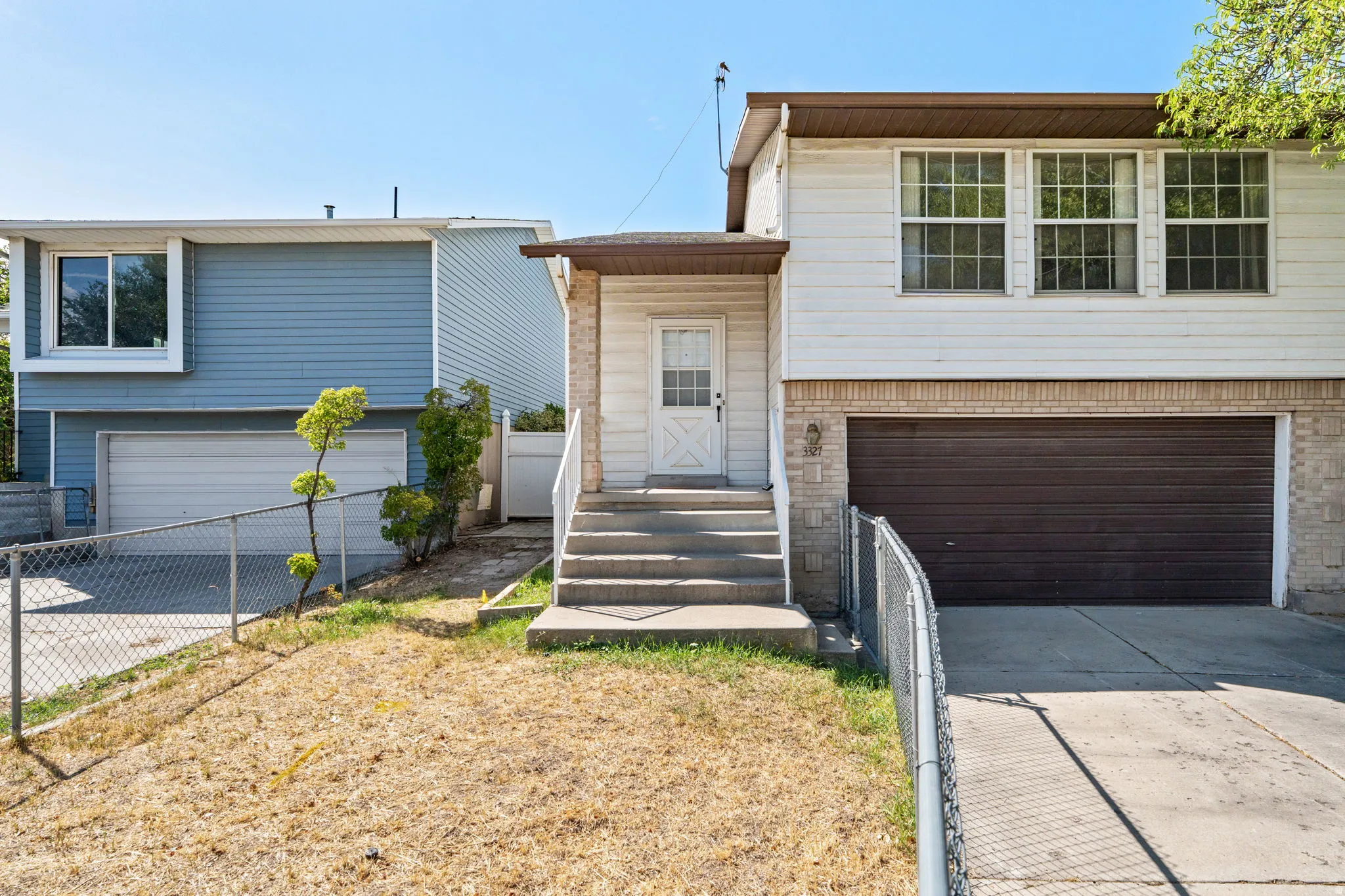 White siding exterior with a brown garage door, concrete driveway, and concrete steps leading to the entrance