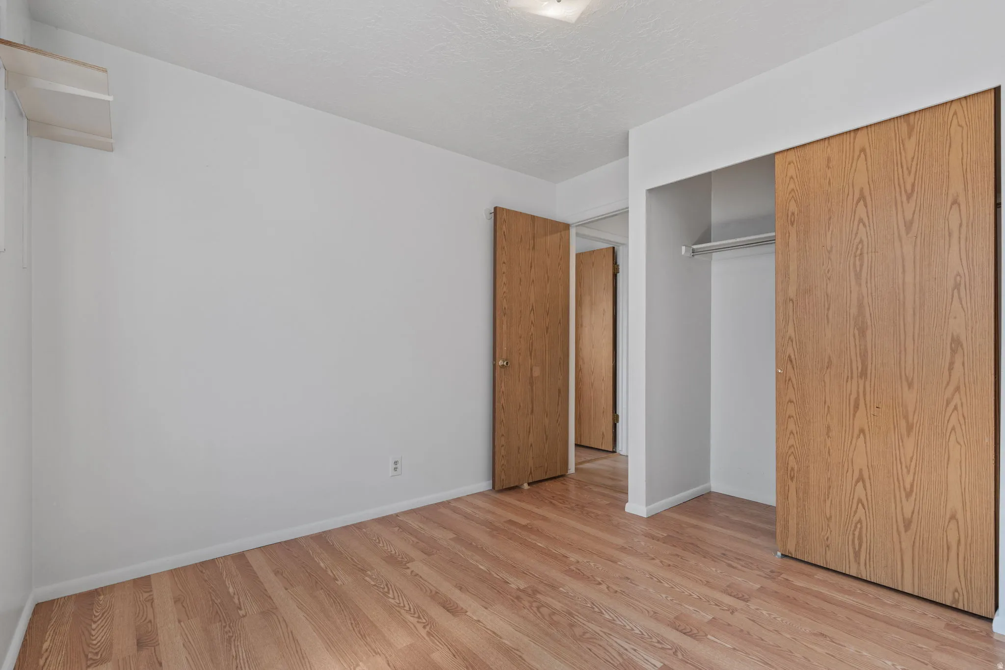 Wood-finish flooring, white walls, and a built-in closet with sliding doors