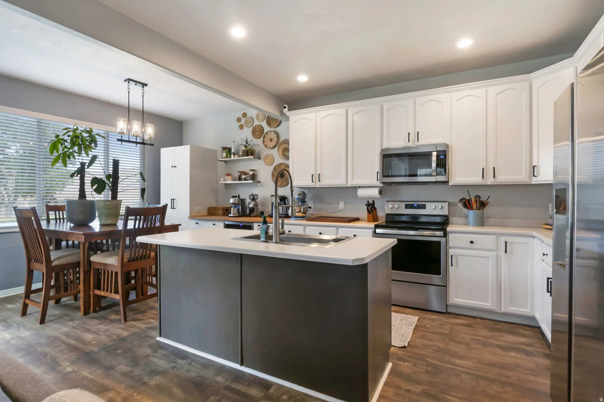 Kitchen featuring stainless steel appliances, white cabinetry, a center island with a sink, wood-finish flooring, and recessed lighting