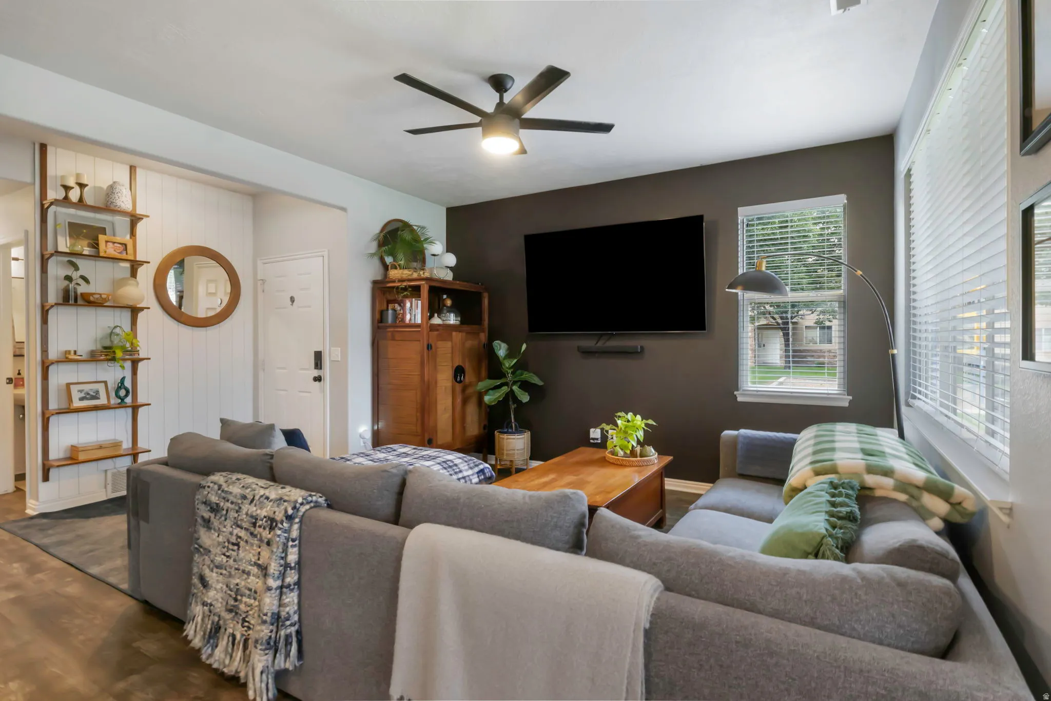 Spacious living area featuring a dark accent wall, wood-finish flooring, and a ceiling fan