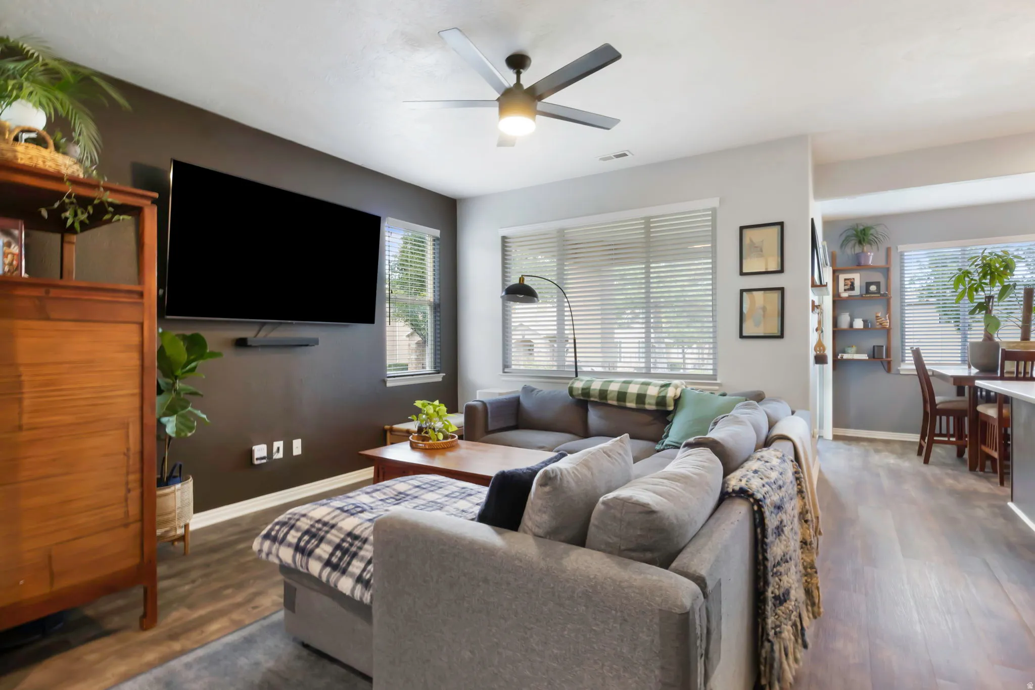 Spacious living area featuring wood-finish flooring, a ceiling fan, and multiple windows with blinds