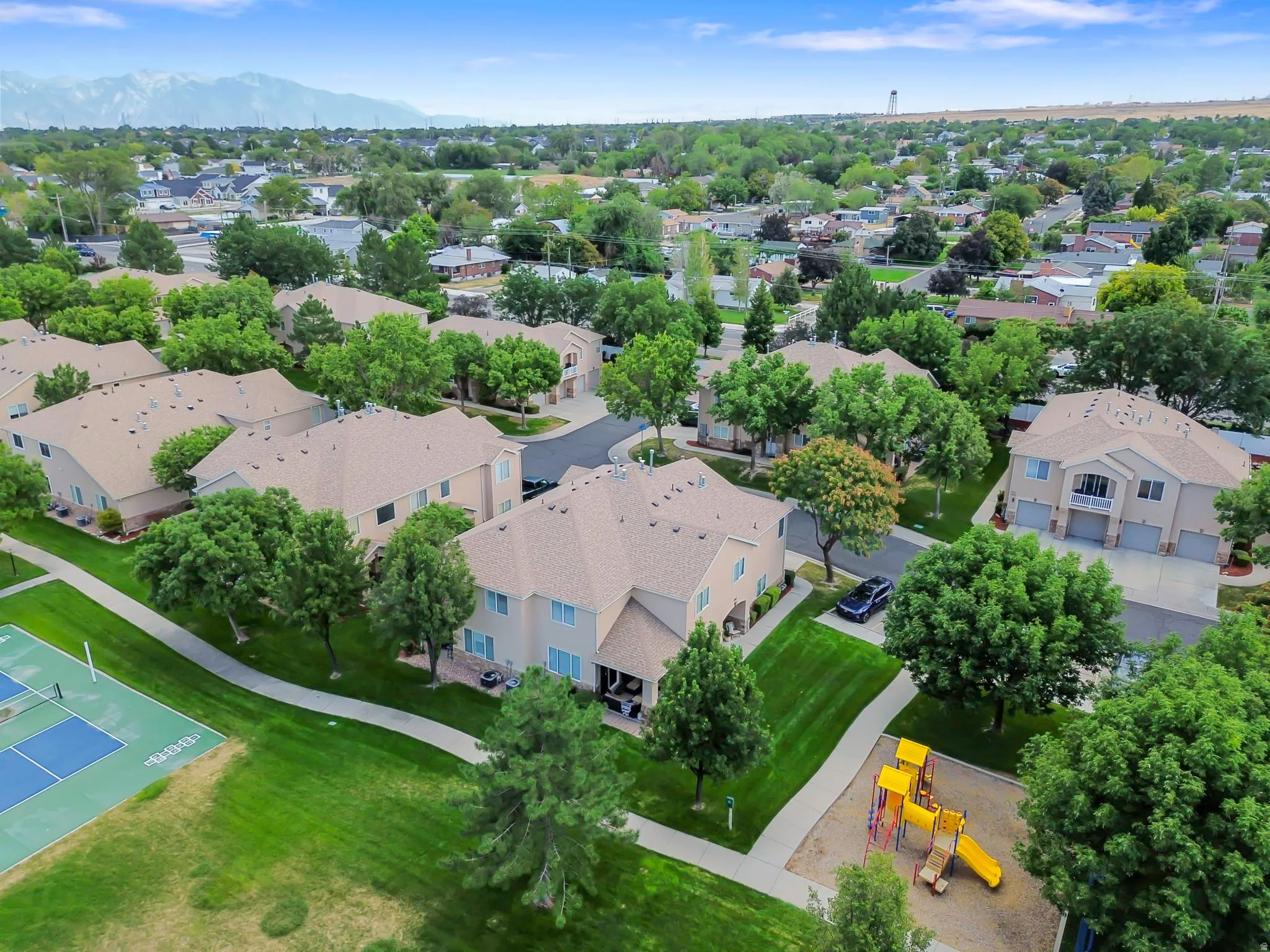 Manicured green spaces, paved walking paths, a playground structure, and a tennis court