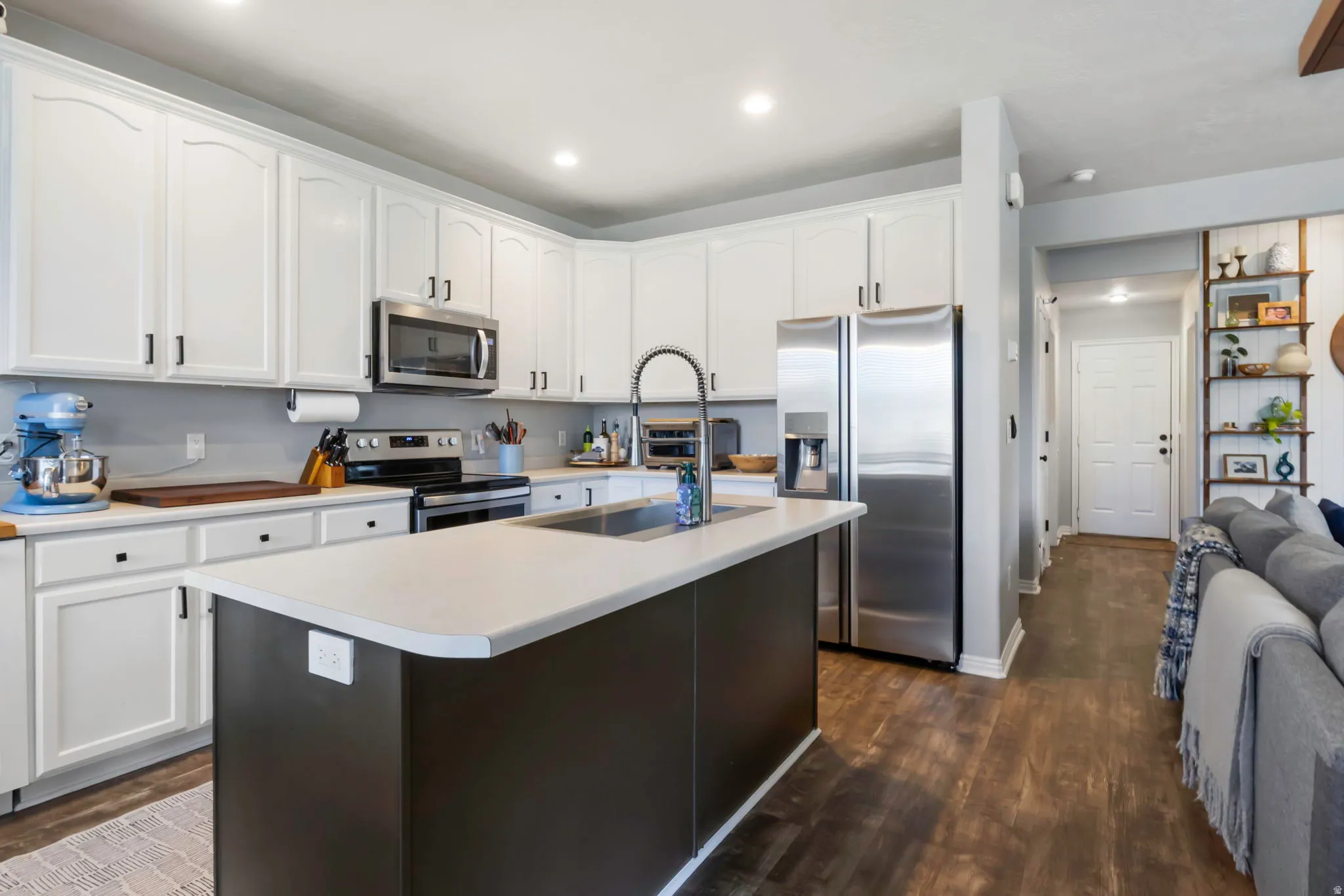 White shaker cabinetry, stainless steel appliances, central island with integrated sink, wood-finish flooring, and recessed lighting
