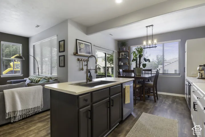 Open-concept living area with wood-finish flooring, a kitchen island with sink, and a dining area featuring a linear chandelier