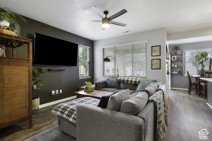 Spacious living area featuring wood-finish flooring, a ceiling fan, and multiple windows with blinds