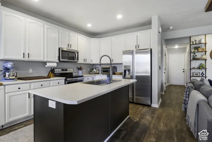 White shaker cabinetry, stainless steel appliances, central island with integrated sink, wood-finish flooring, and recessed lighting