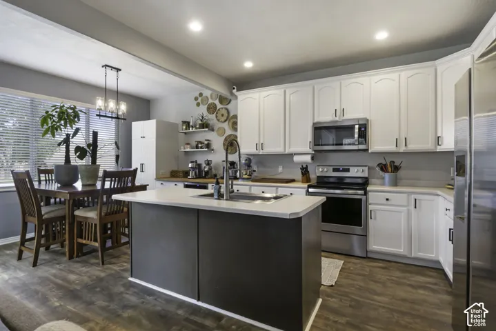 Kitchen featuring stainless steel appliances, white cabinetry, a center island with a sink, wood-finish flooring, and recessed lighting