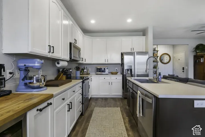 Kitchen featuring white upper and lower cabinetry, stainless steel appliances, and a large island with an undermount sink