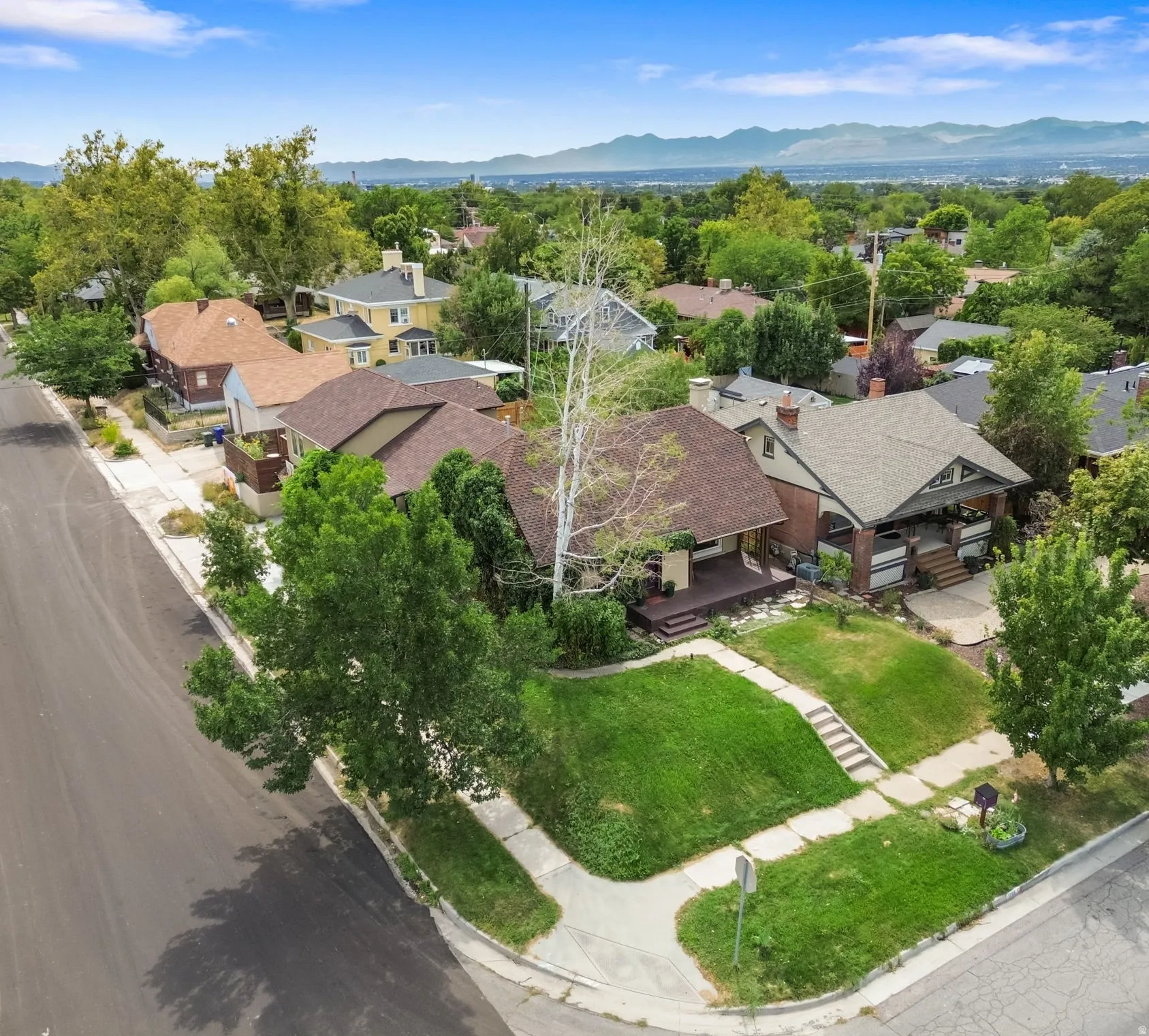 Street-facing property with a corner lot, mature trees, and a terraced front yard