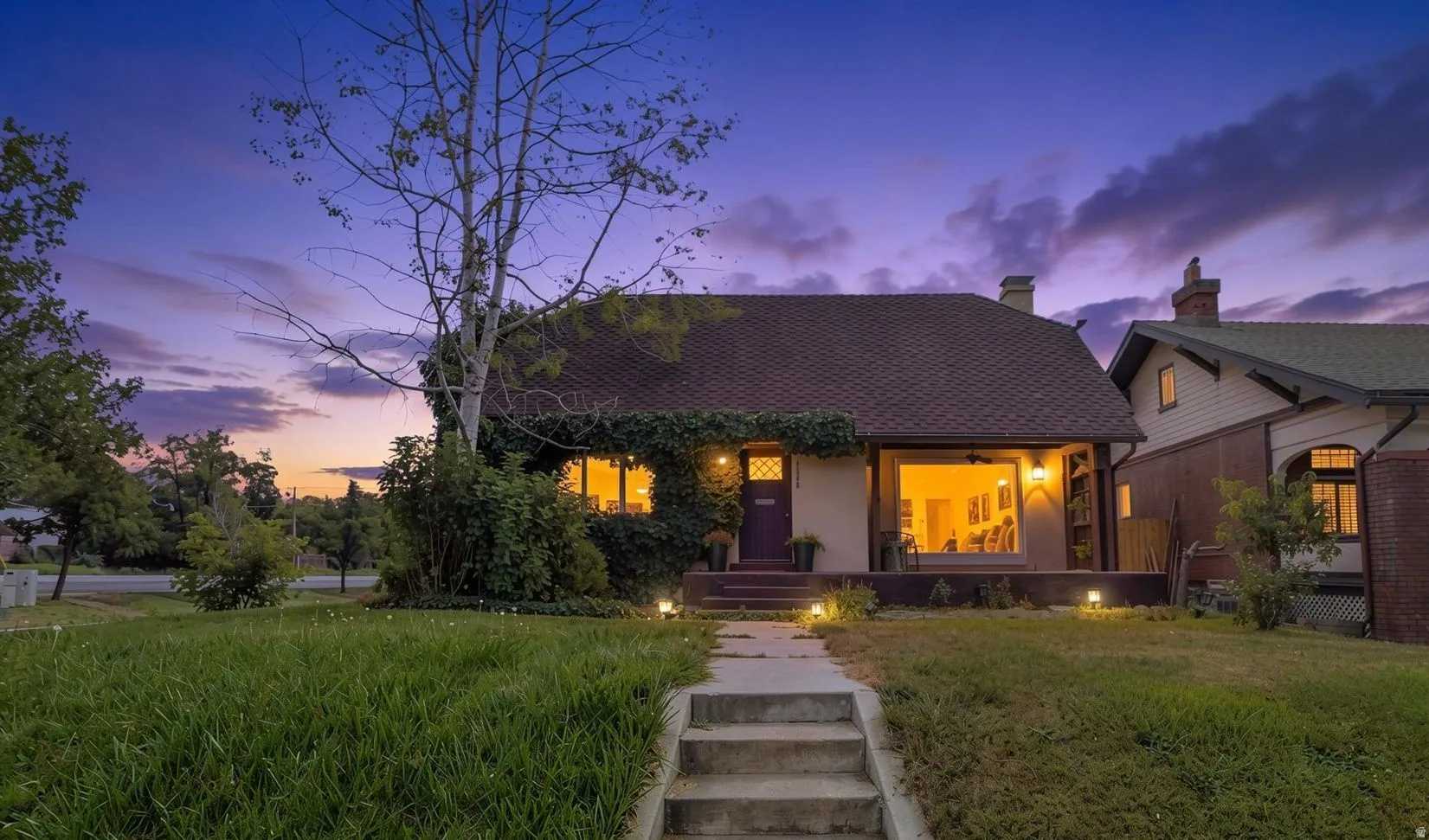Cottage-style residence with a distinct front door, covered entry, expansive front window, and a concrete walkway with integrated lighting