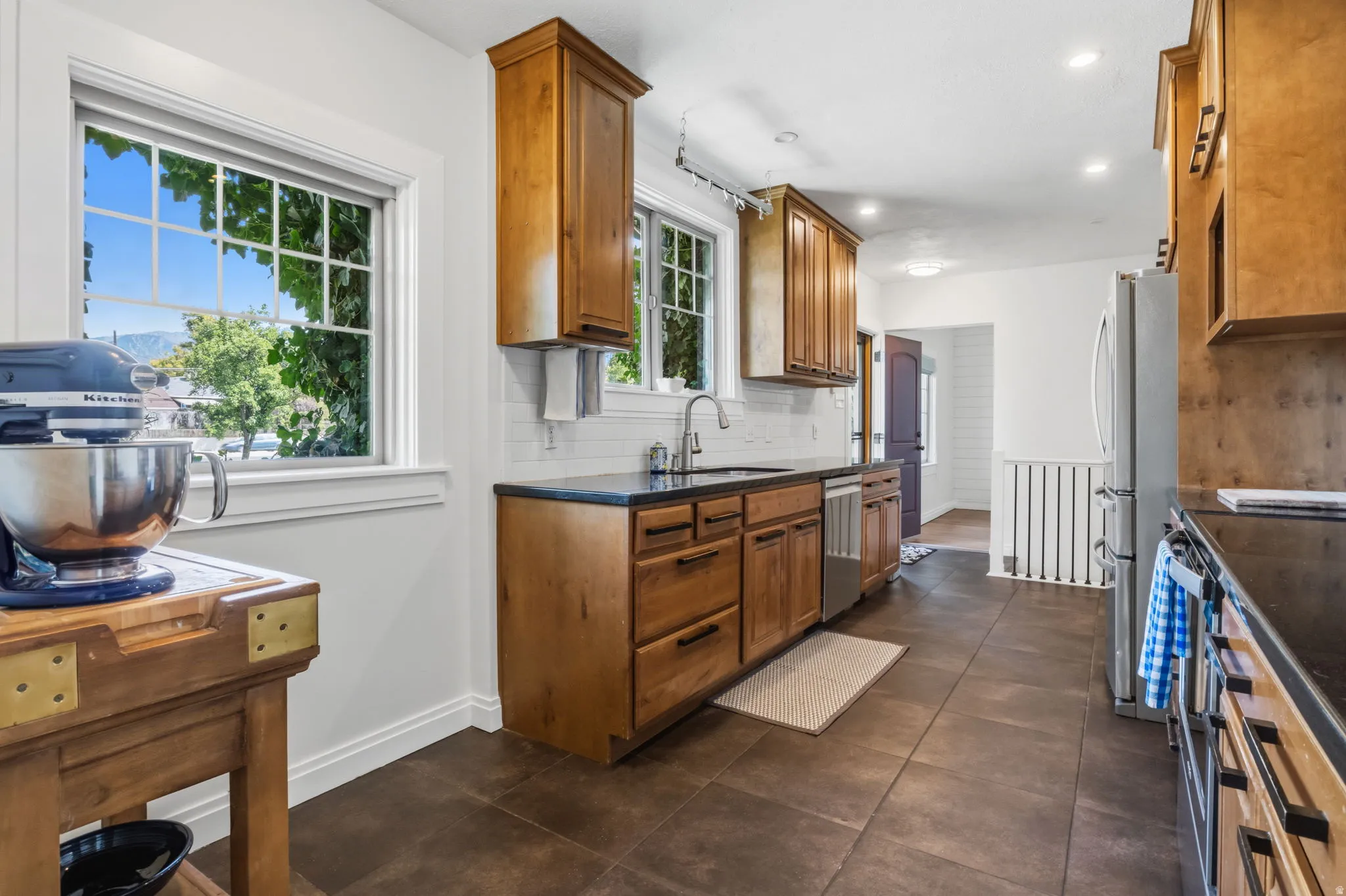 Kitchen with wood cabinetry, dark countertops, a tile backsplash, stainless steel appliances, and large window