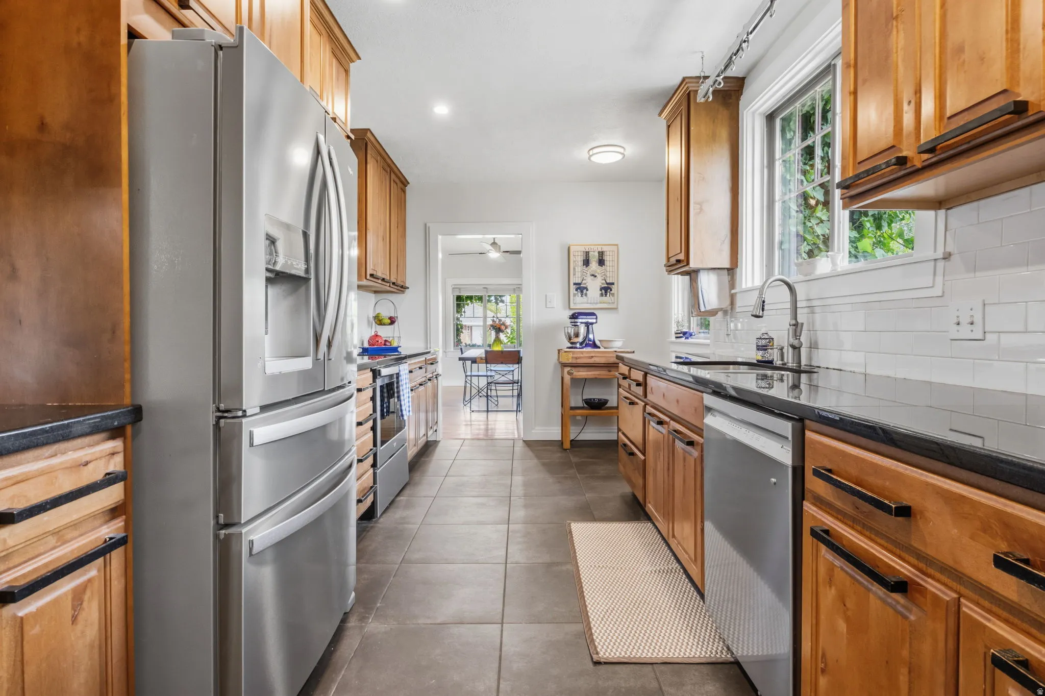 Stainless steel appliances, wood cabinetry, dark countertops, tile flooring, and a subway tile backsplash