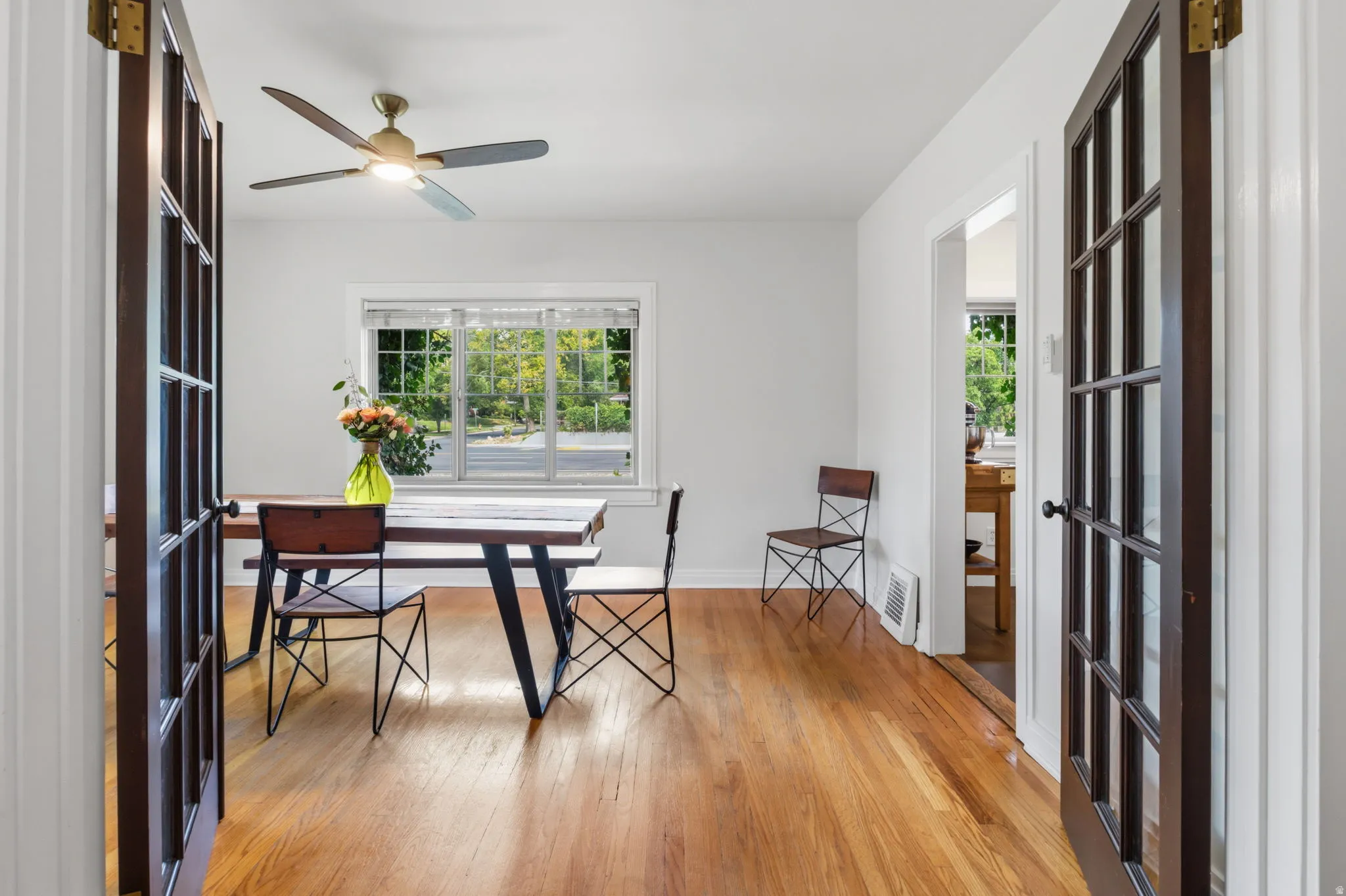 Hardwood flooring, multi-pane French doors, ceiling fan with integrated lighting, and a large window with privacy blinds