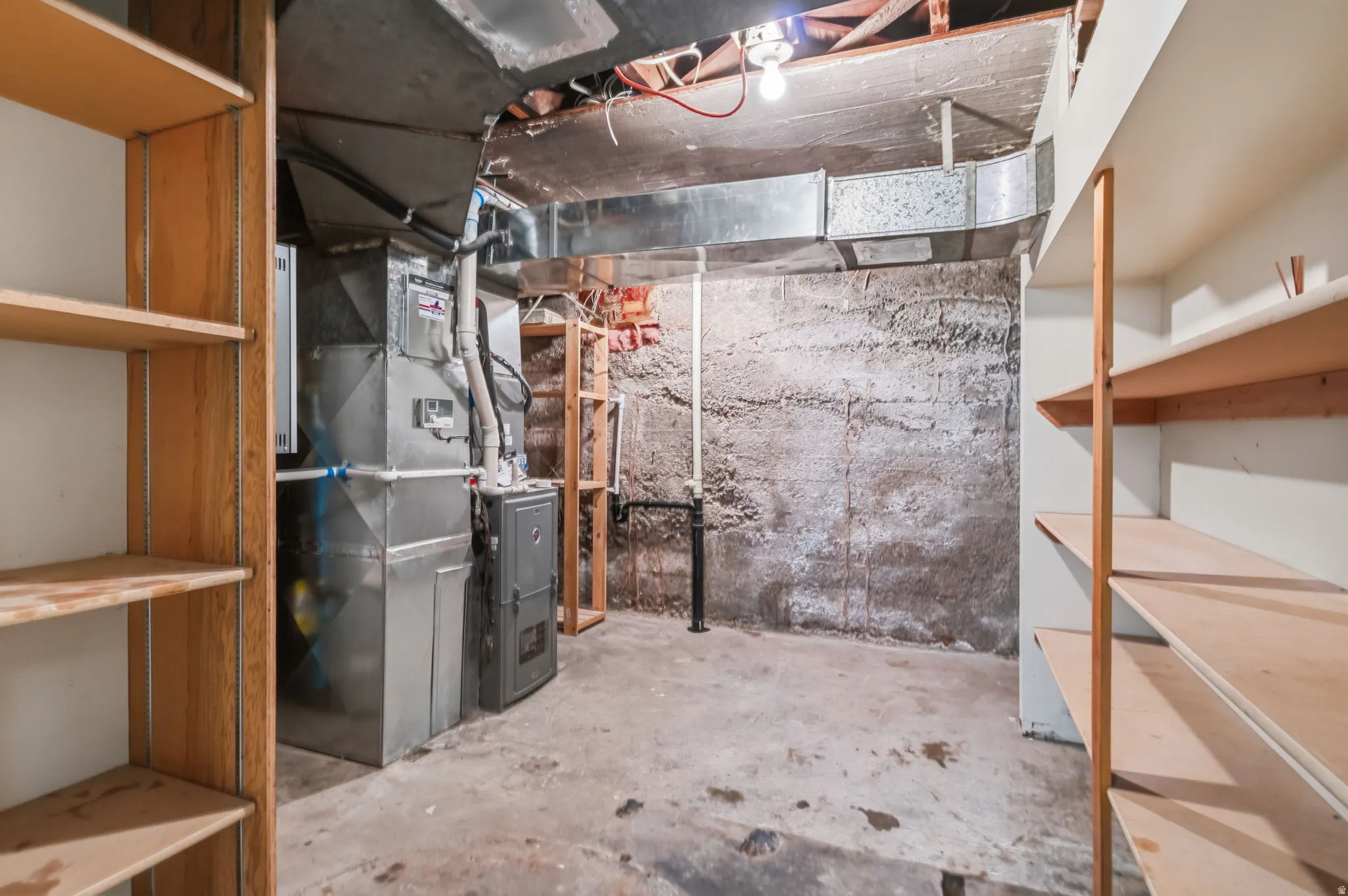 Unfinished basement with concrete flooring and exposed ceiling, featuring built-in wooden shelving units