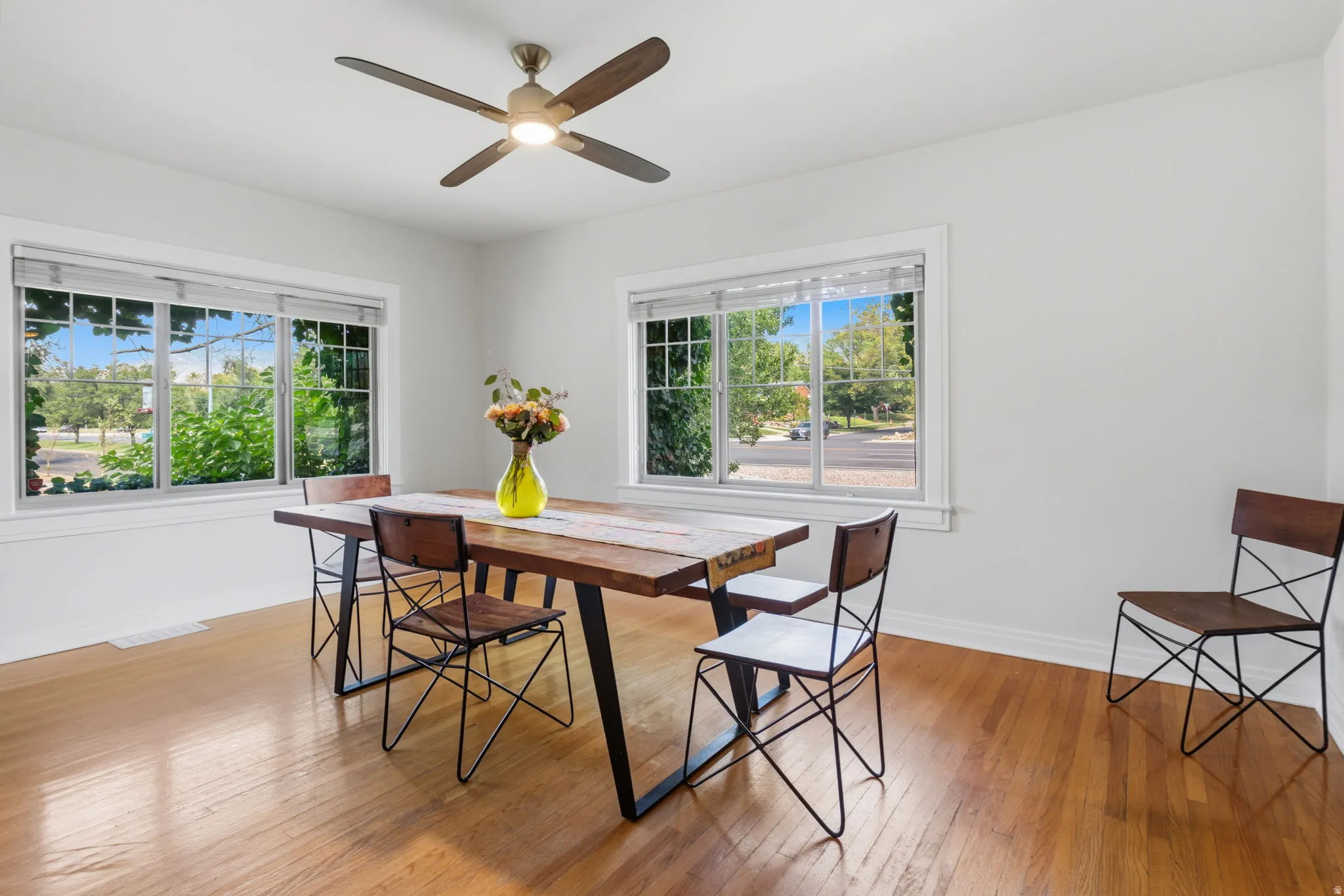 Hardwood flooring, white painted walls, white window trim, and a ceiling fan with integrated lighting