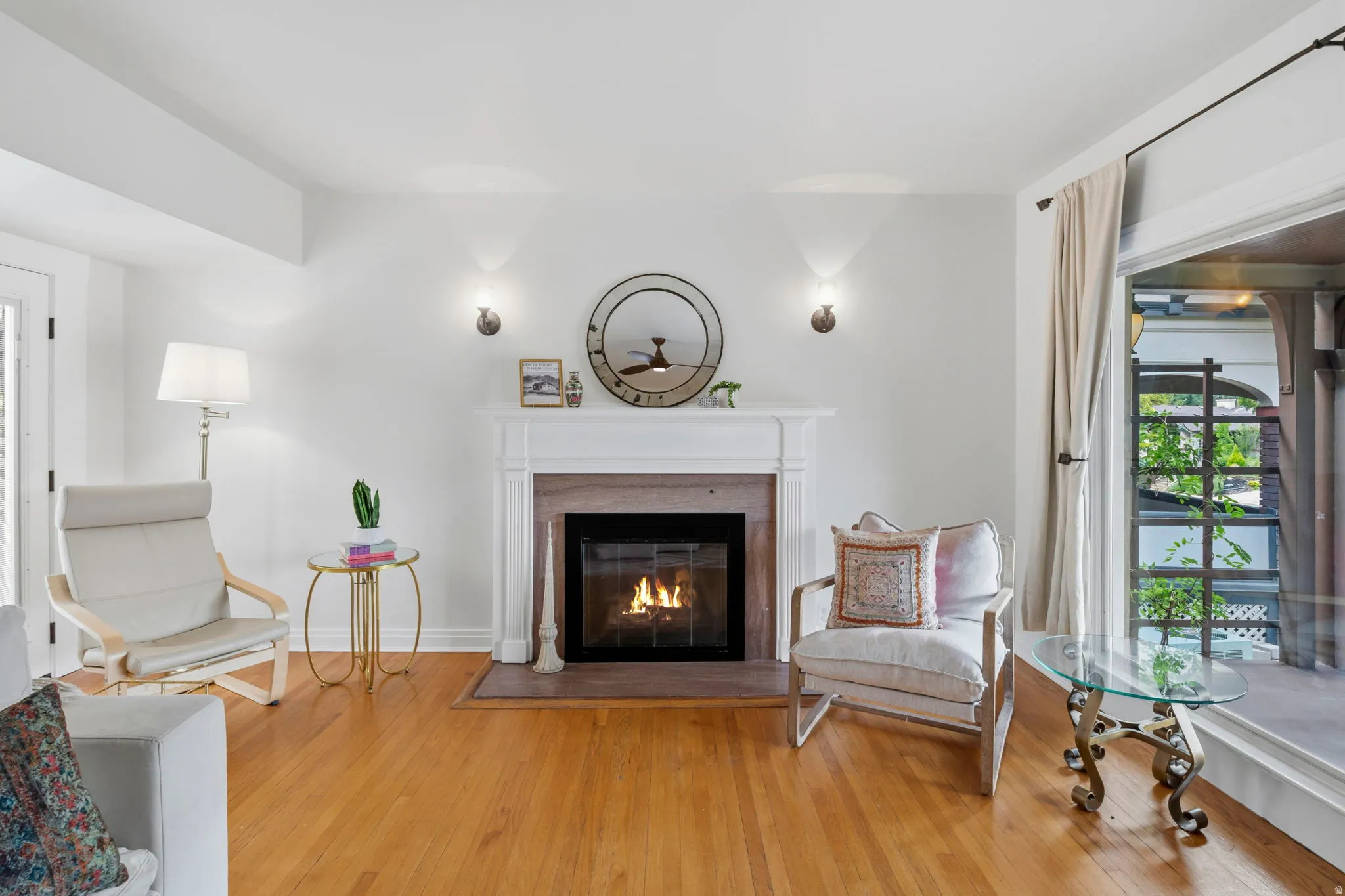 Hardwood flooring, a white mantel, an integrated fireplace, and wall-mounted sconces