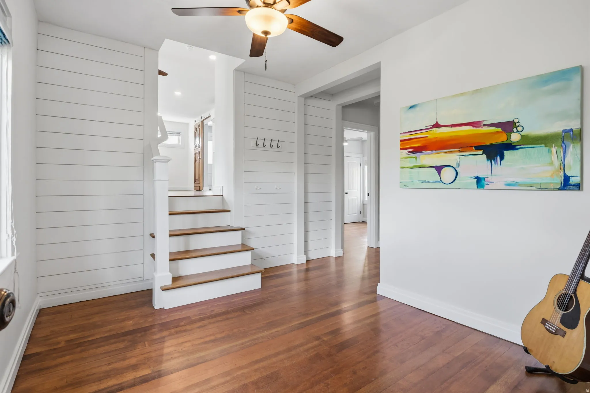Up to Primary suite Hardwood flooring, shiplap wall accents, staircase with wood treads, ceiling fan with integrated lighting, and white trim