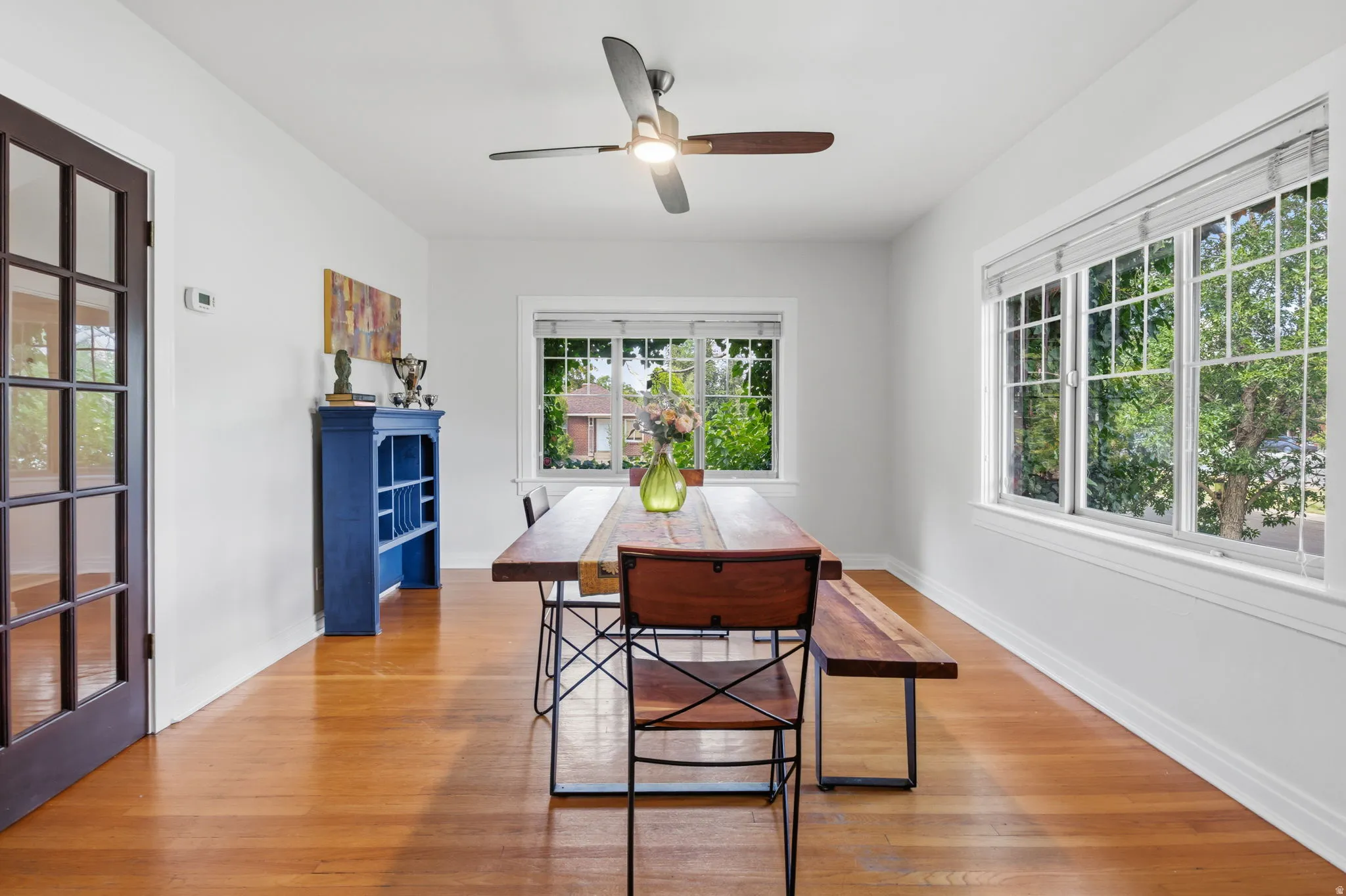 Hardwood flooring throughout, multiple windows with natural light, ceiling fan with integrated lighting, and a glass-paneled interior door