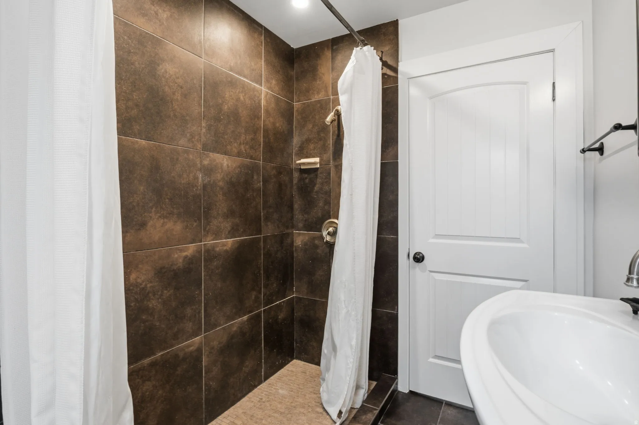 Shower with dark brown tile surround, brushed nickel fixtures, and recessed lighting