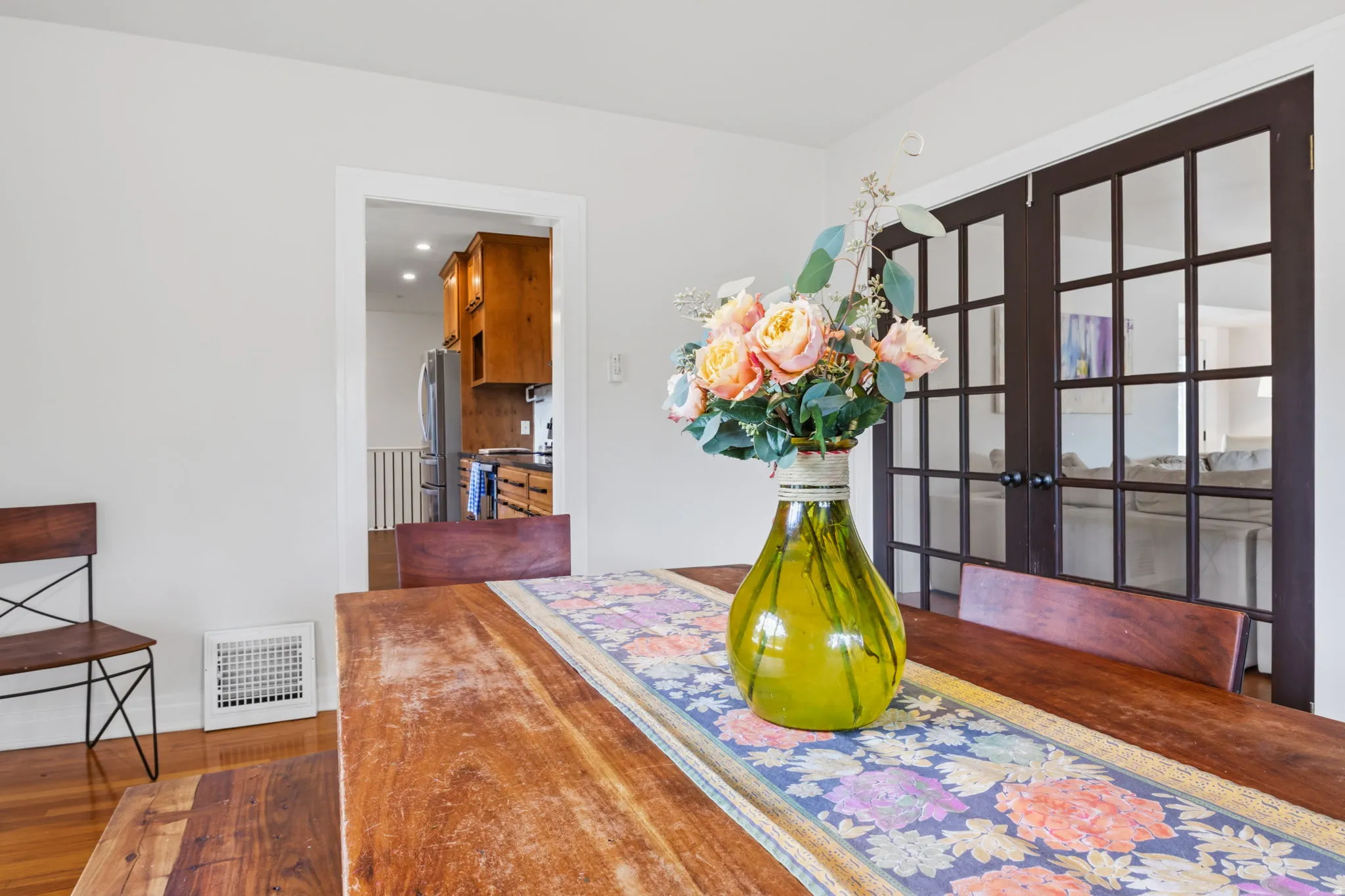 Hardwood flooring, painted walls, white trim, and a doorway to the kitchen with wood cabinetry and a stainless steel refrigerator