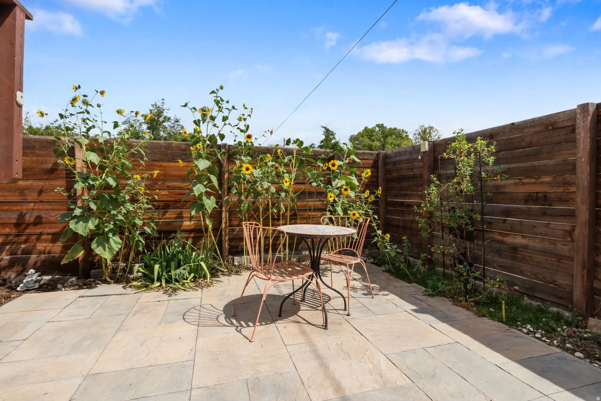 Paved patio area with stone-finish pavers, surrounded by a horizontal wood plank fence and garden plantings