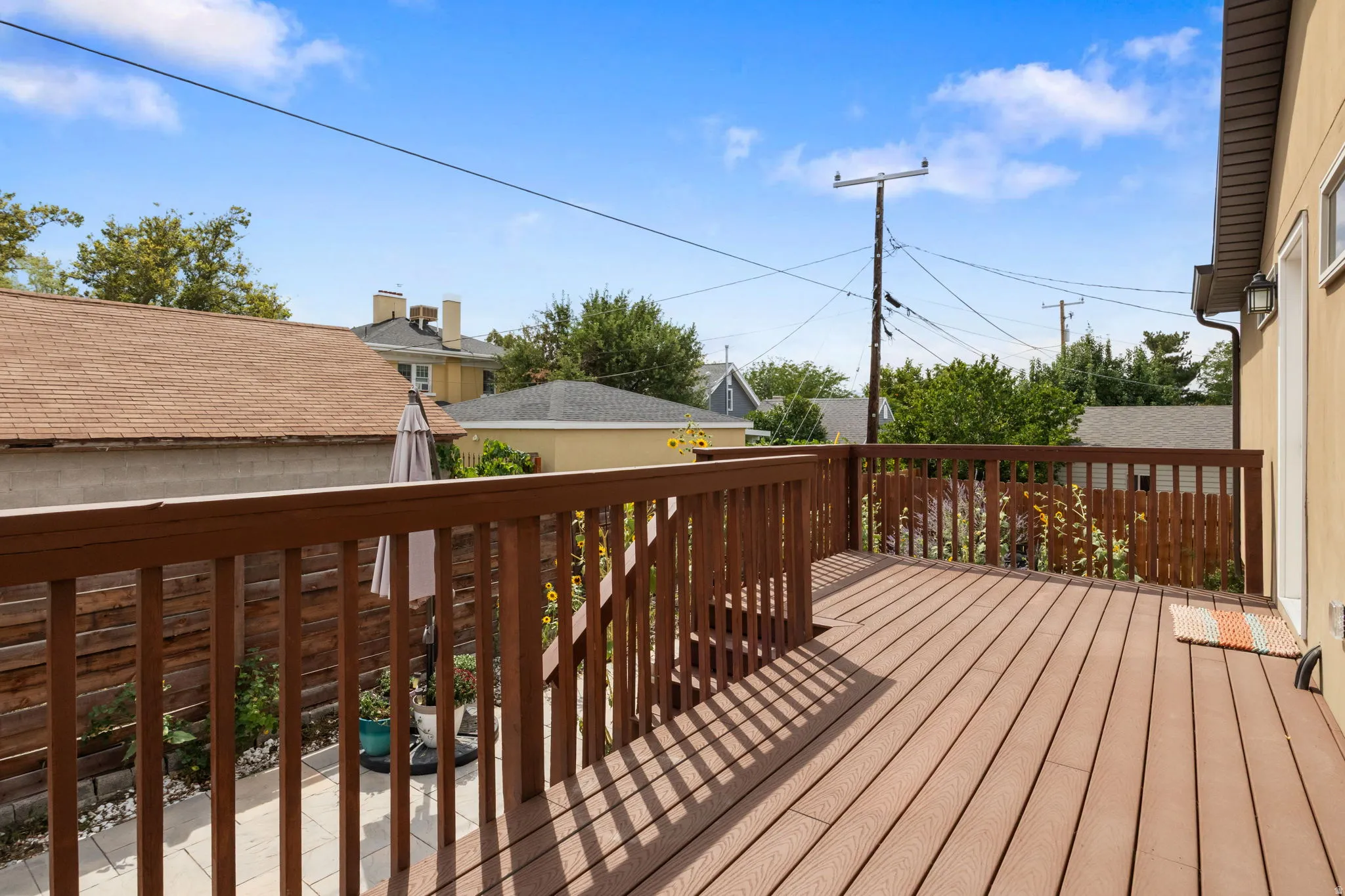 Expansive wood-finish deck with a brown railing, exterior lighting, and a stucco-finish wall