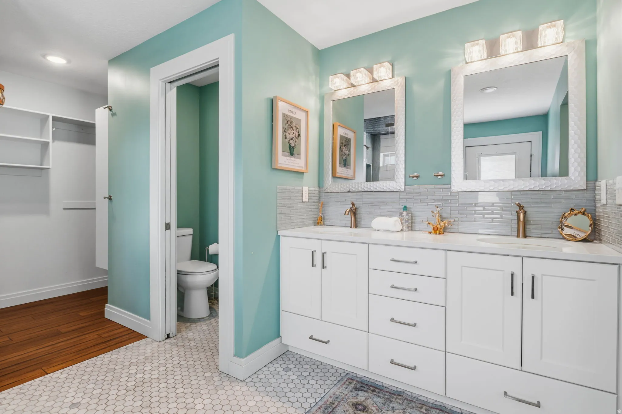 Dual vanity with integrated sinks, white cabinetry, hexagon tile flooring, and a walk-in closet with built-in shelving