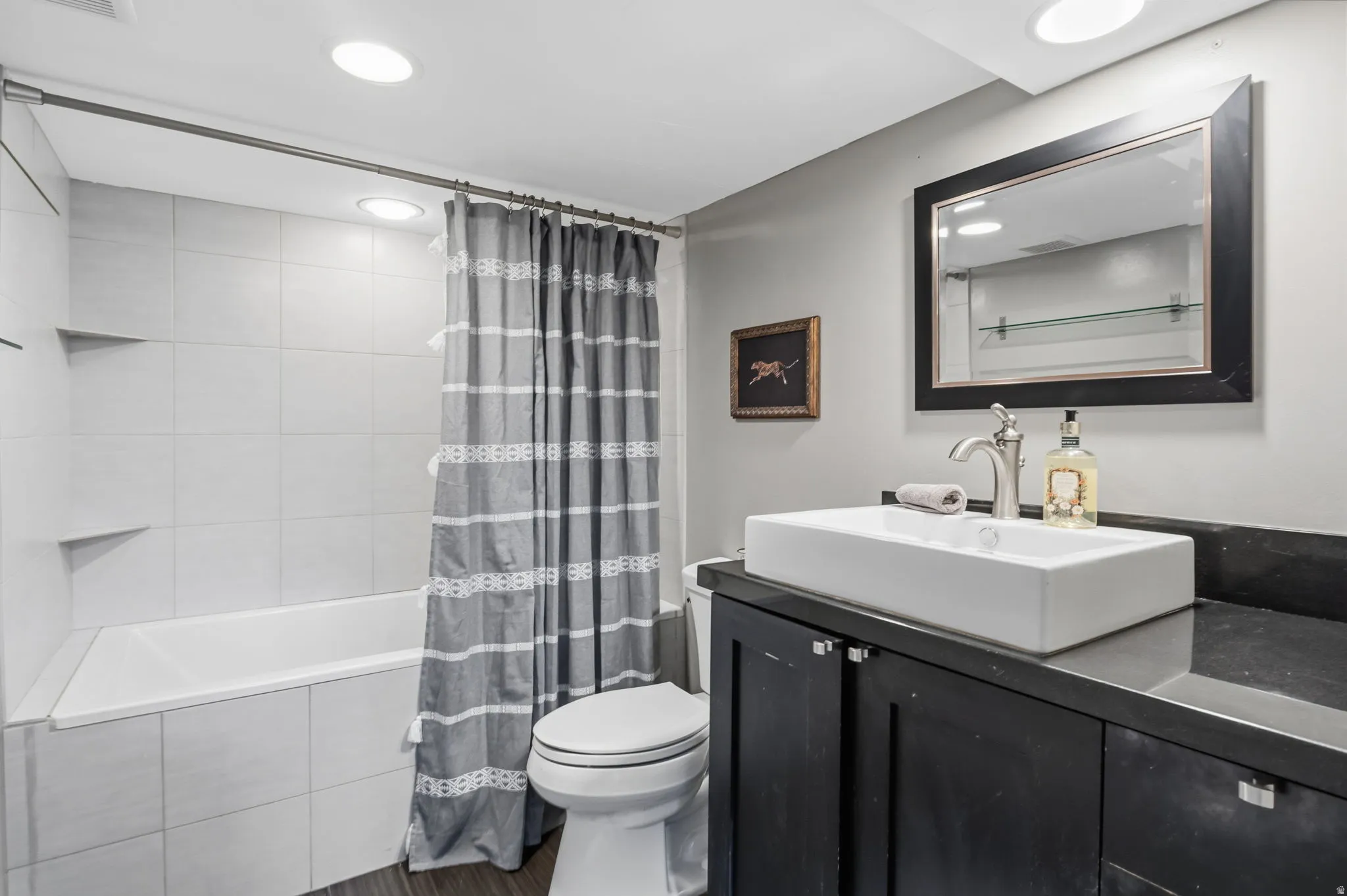White tiled bath and shower combination with recessed shelving in basement bathroom