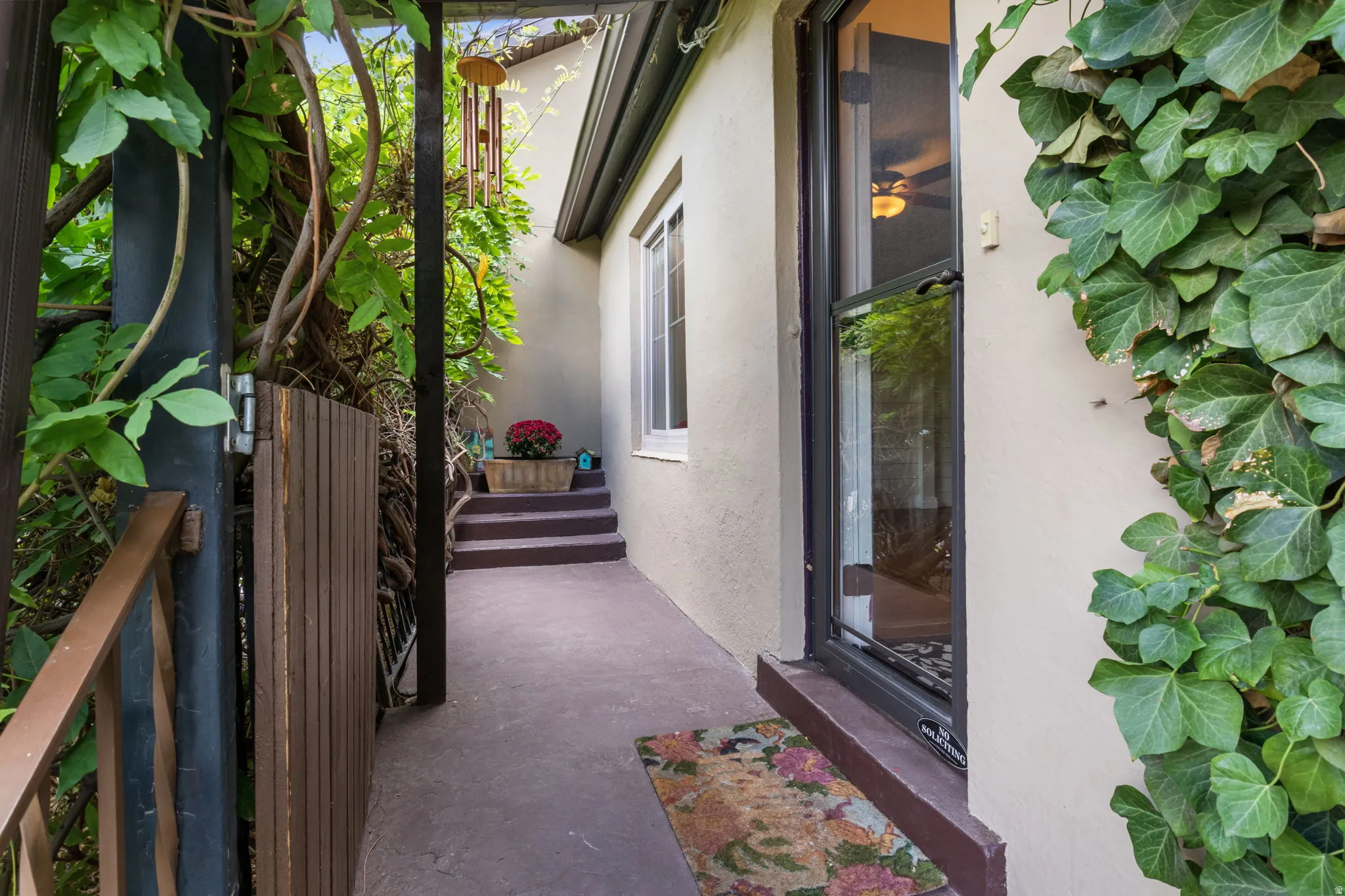 Stucco exterior with ivy accents, wood privacy gate, concrete walkway, and a glass-paneled entry door