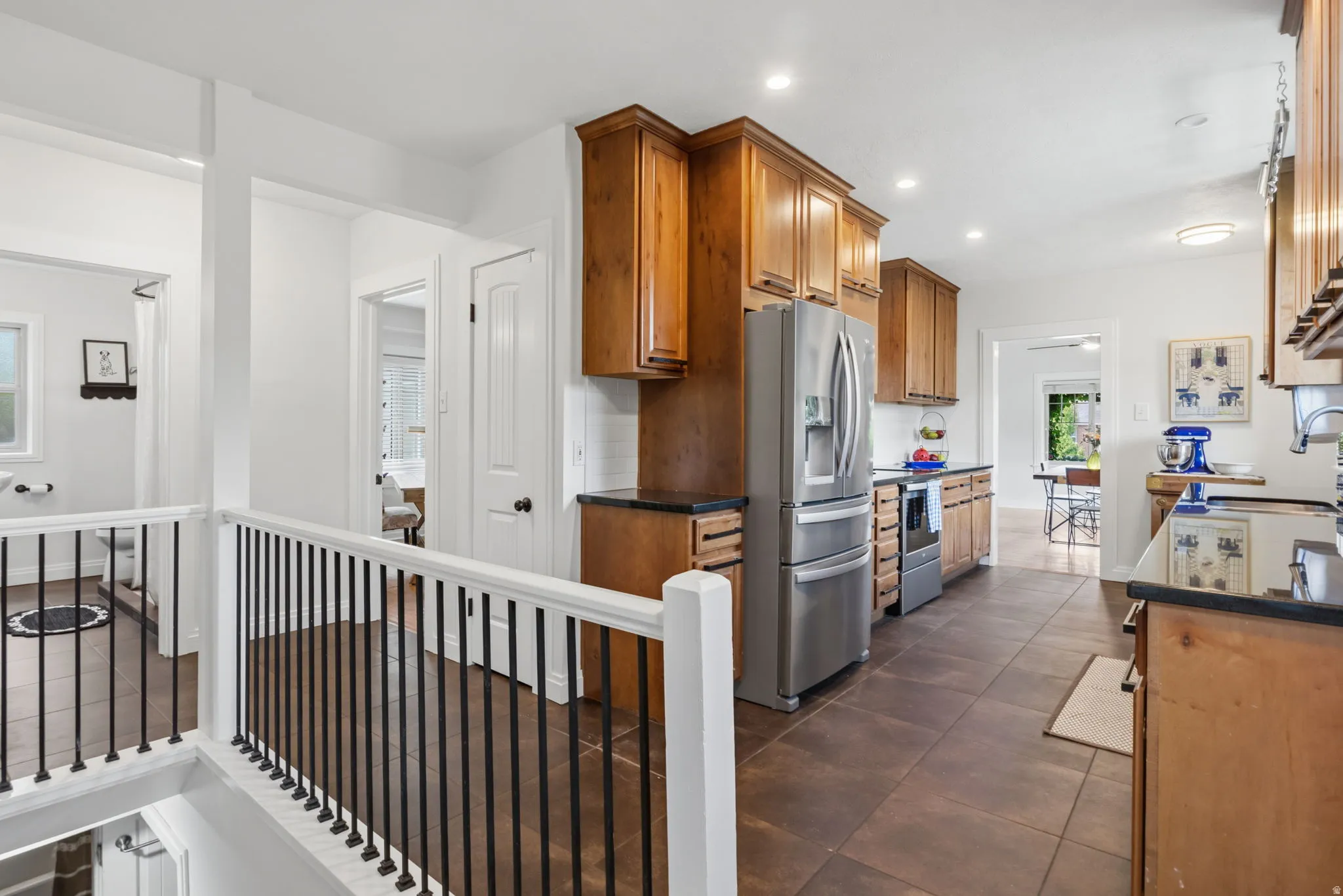 Stainless steel appliances, recessed lighting, wood-finish cabinetry, dark countertops, and tile flooring