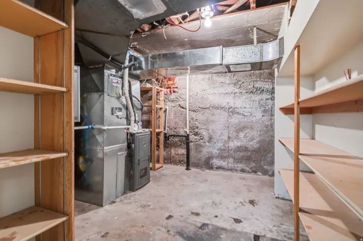 Unfinished basement with concrete flooring and exposed ceiling, featuring built-in wooden shelving units