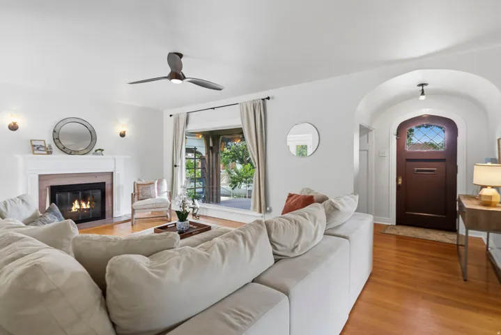 Hardwood flooring throughout, a white mantel fireplace, and a ceiling fan with integrated lighting